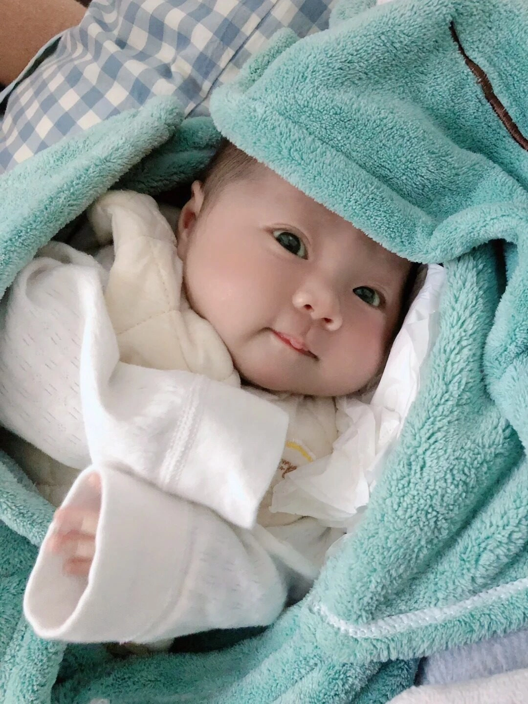 Mỉm cười nhẹ nhàng, bé yêu ấm áp trong chiếc chăn xanh đáng yêu.