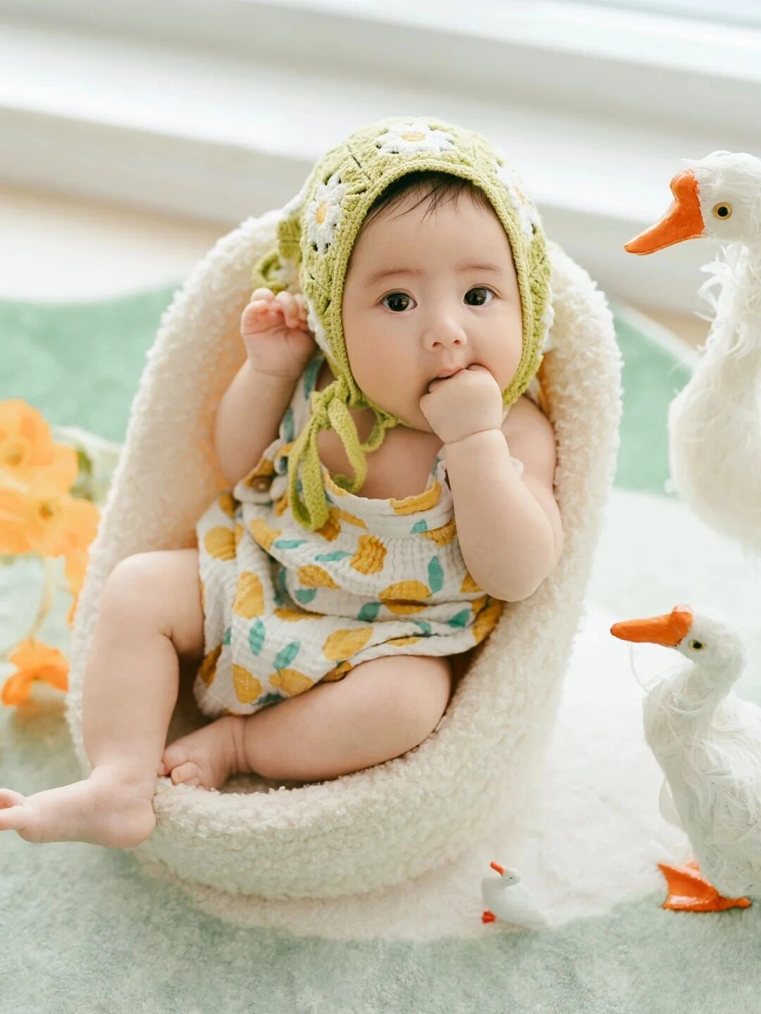 Bé ngồi trong ghế bông mềm, tay ngậm miệng như đang suy tư.