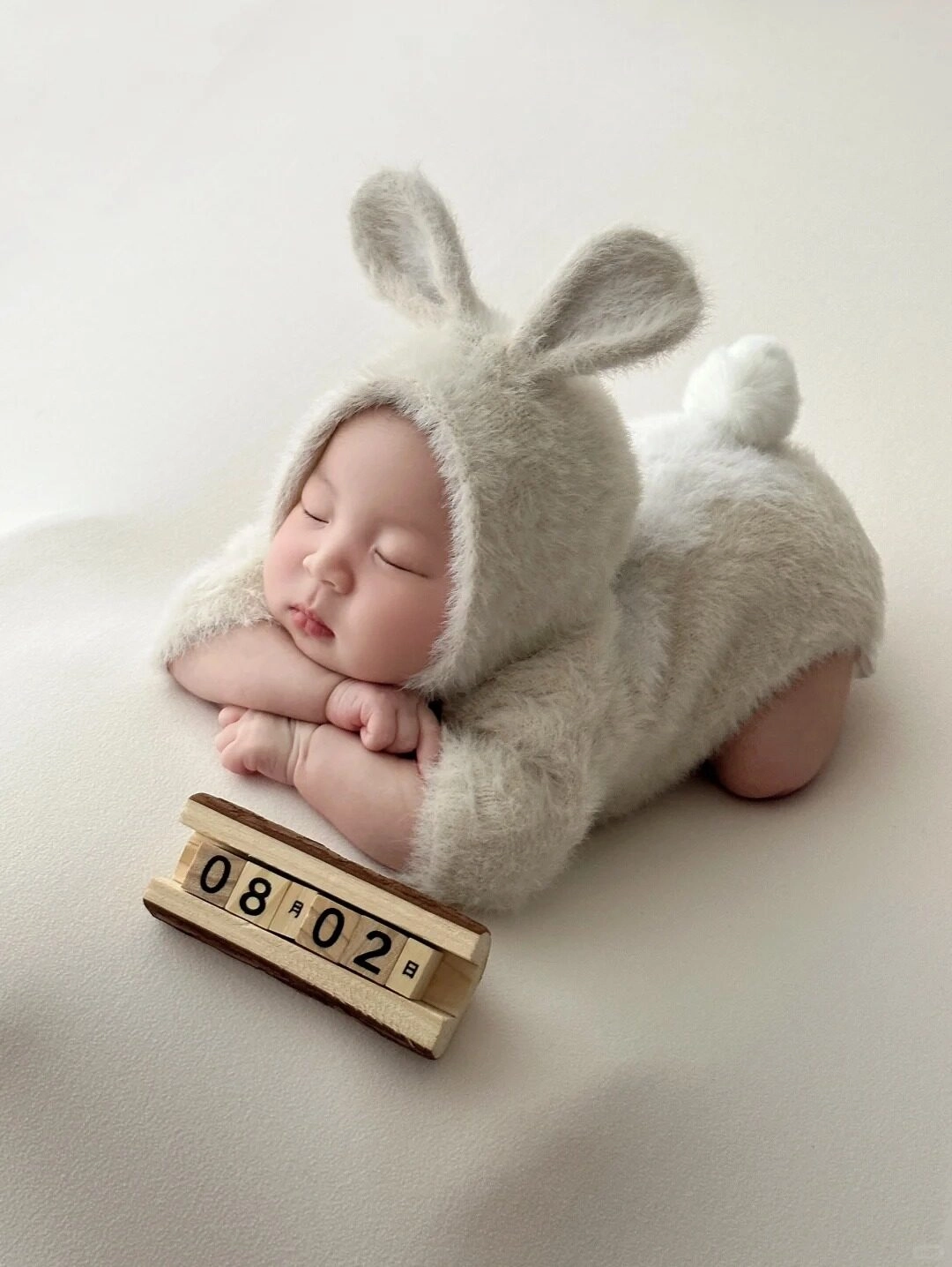 Bé diện bộ đồ thỏ bông mềm mại, nằm ngủ ngon lành trên nền trắng.