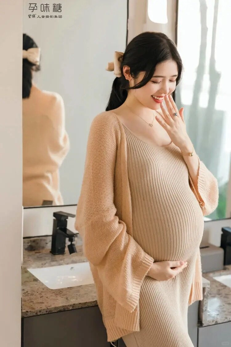 Váy len dài mềm mại, tay nhẹ đặt lên bụng bầu, ánh mắt đầy yêu thương.