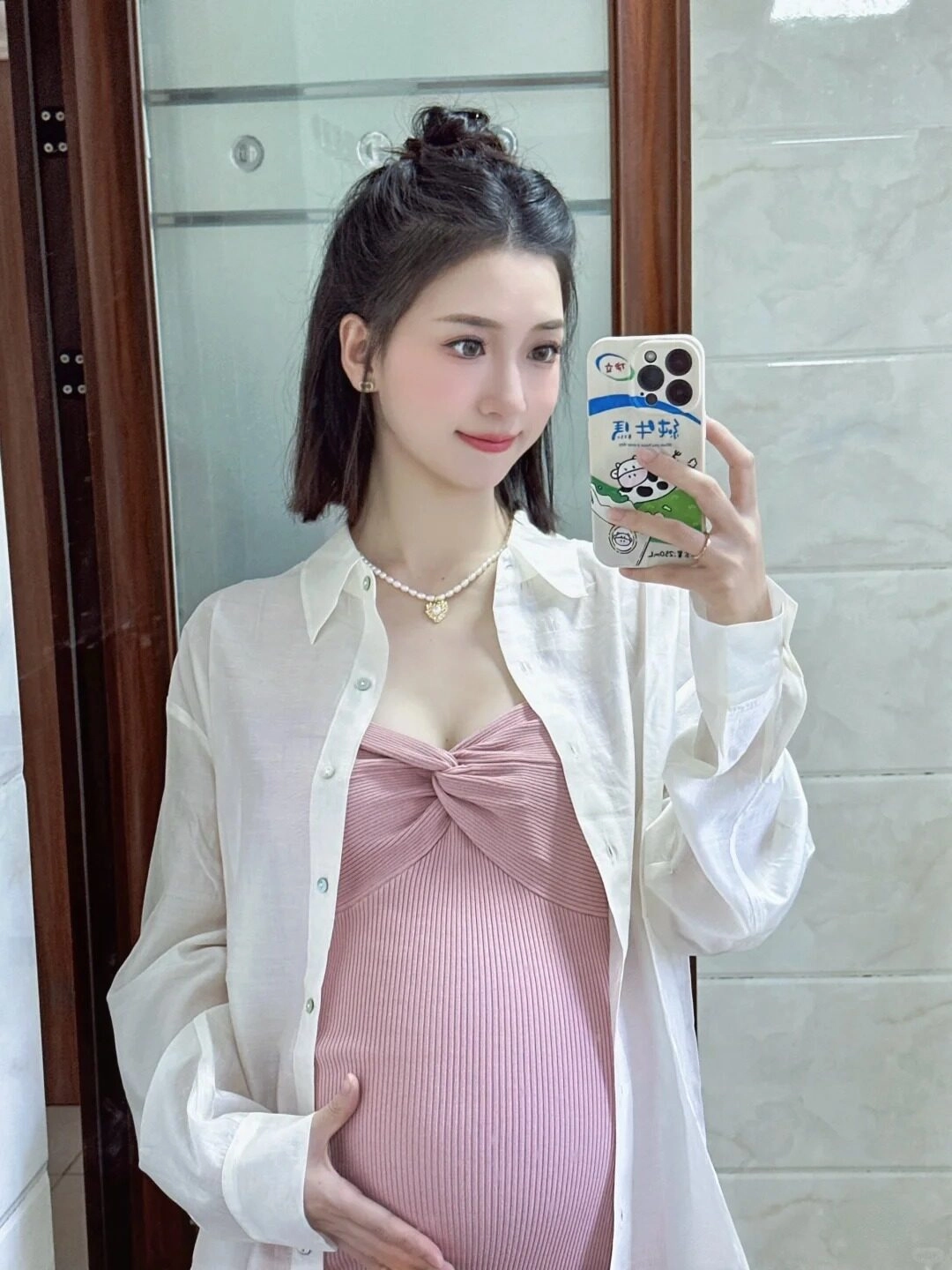 Váy hồng nơ trước phối sơ mi trắng rộng, mẹ bầu dịu dàng trước gương.