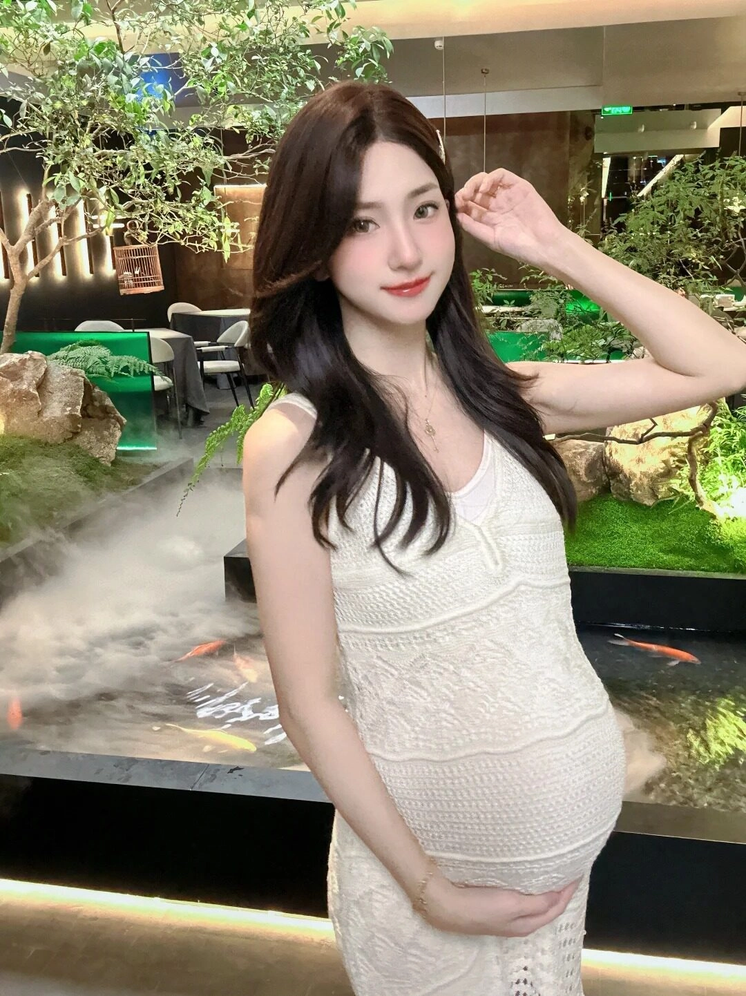 Váy maxi ren trắng mềm mại, mẹ bầu rạng rỡ giữa không gian nhà hàng xanh mát.