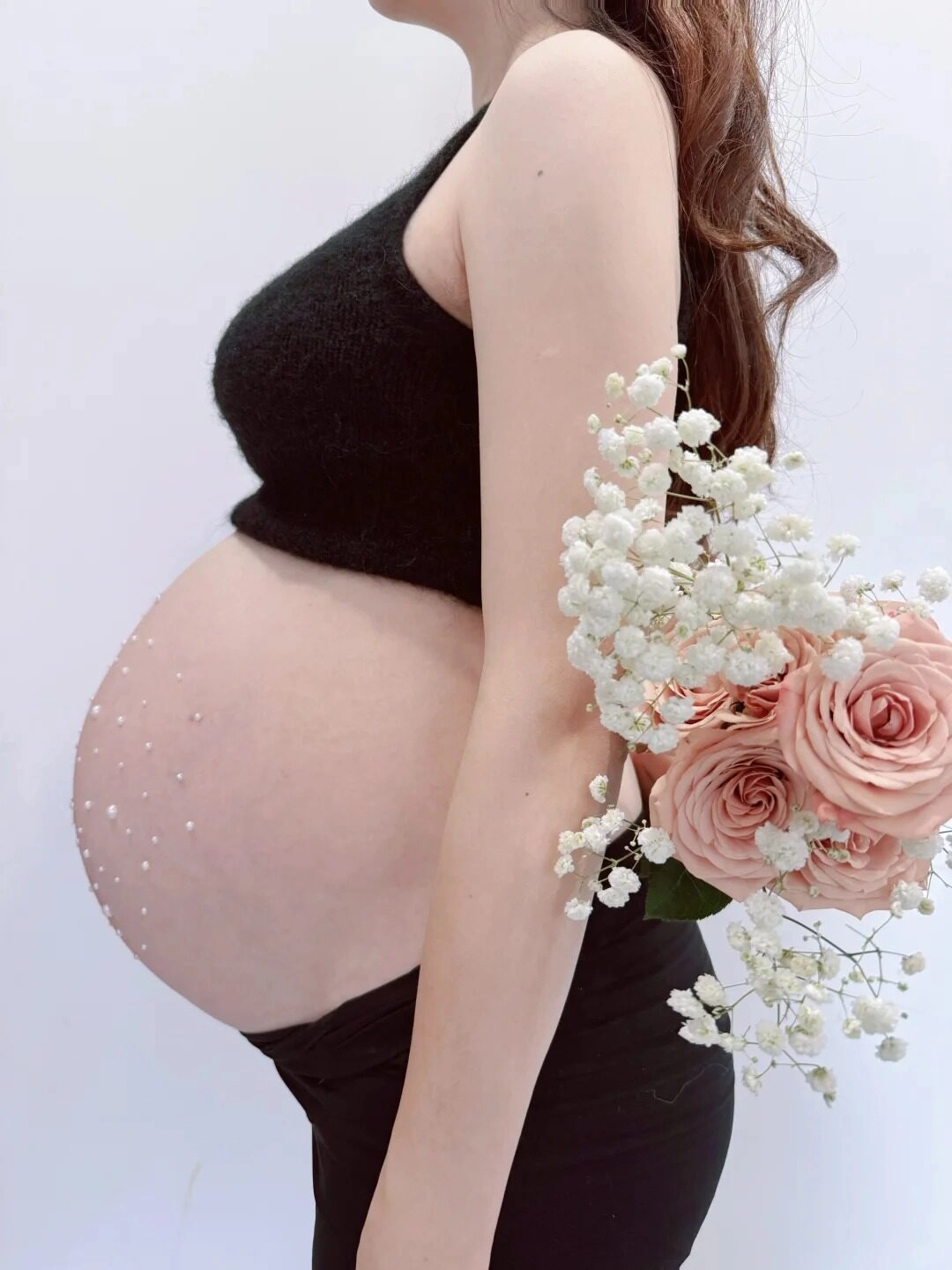 Chân váy đen, áo croptop lông phối ngọc trai, tay cầm bó hoa nhẹ nhàng.