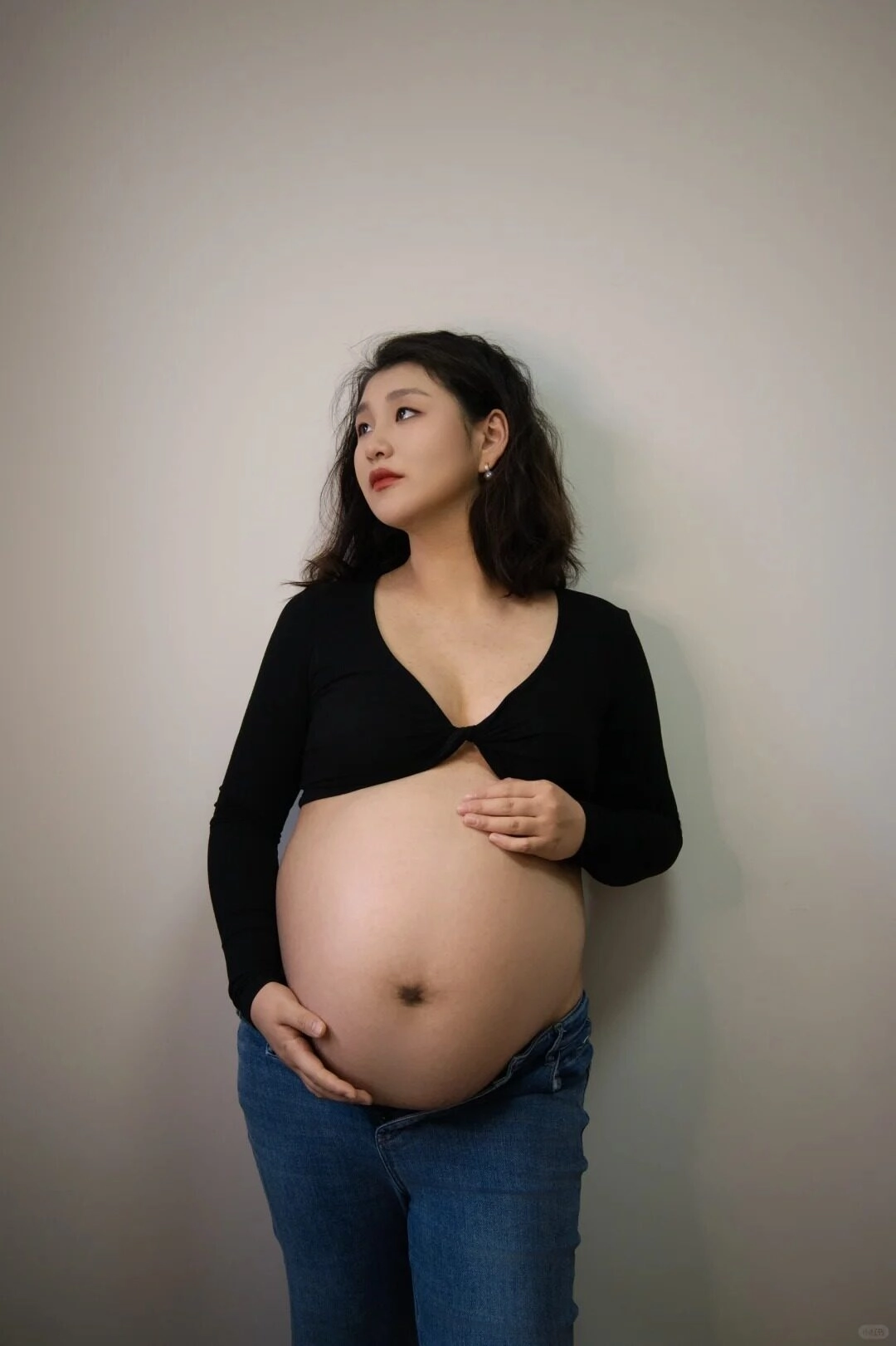 Áo croptop đen kết hợp quần jeans, tay cô gái nhẹ nhàng chạm bụng bầu.
