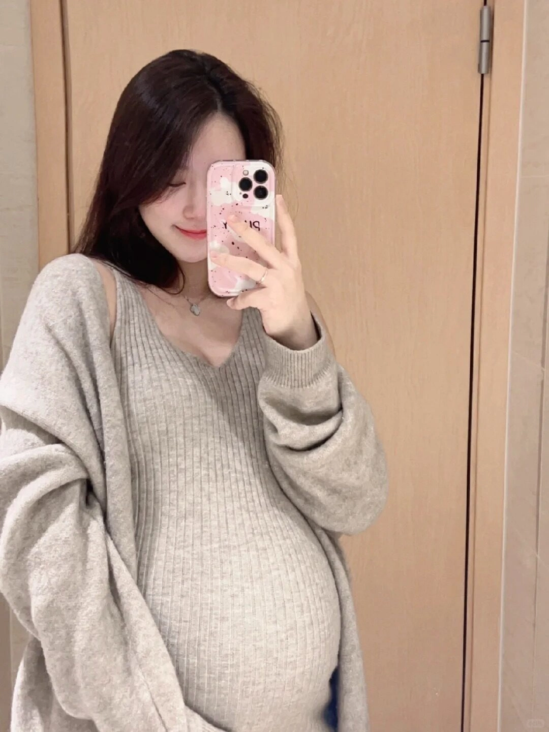 Áo len dài xám nhẹ nhàng khoác ngoài, bàn tay cô gái đặt lên bụng bầu.