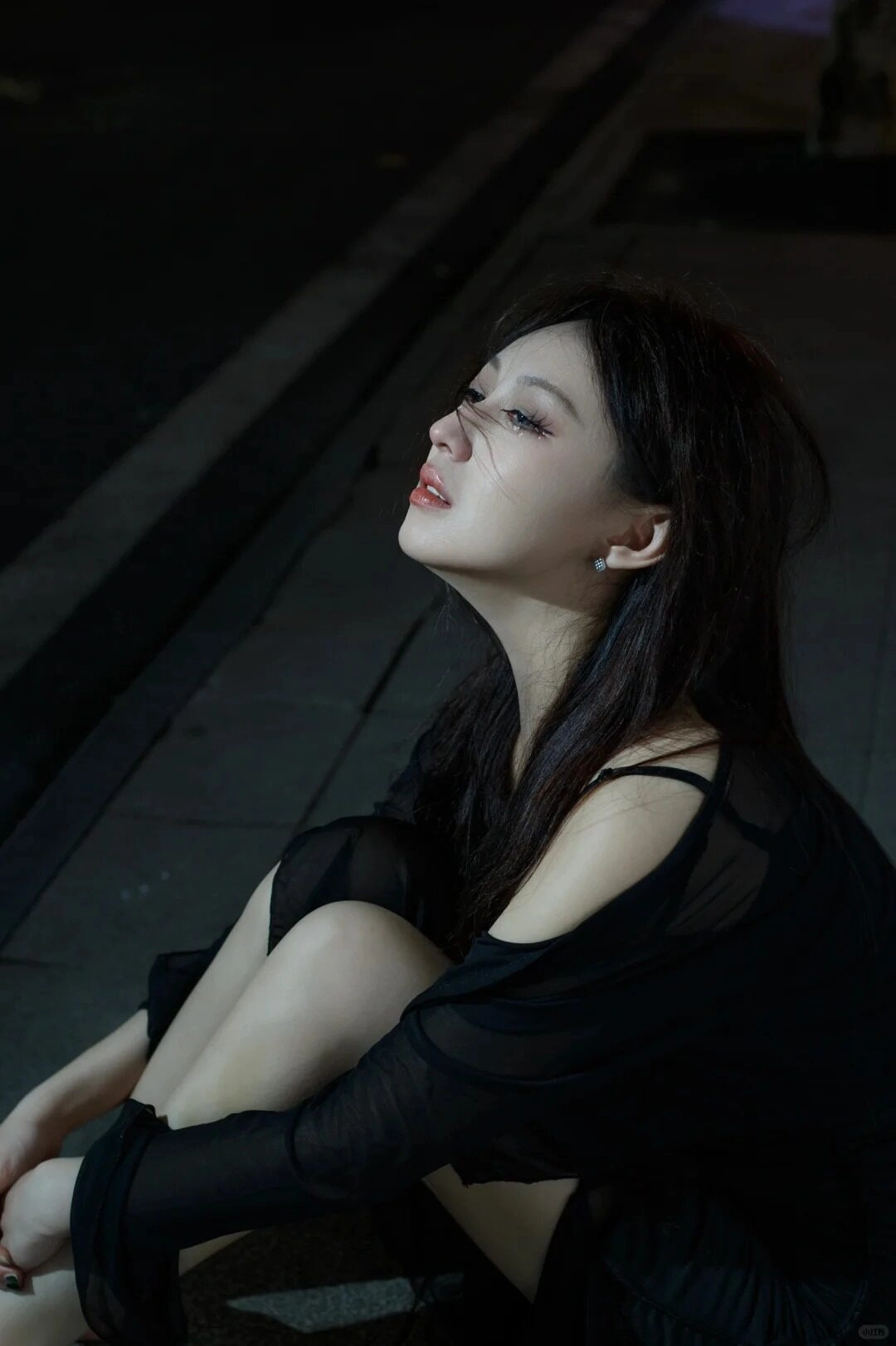 Cô gái ngồi trên vỉa hè với đôi mắt buồn vời vợi, ánh đèn phố nhạt nhòa.