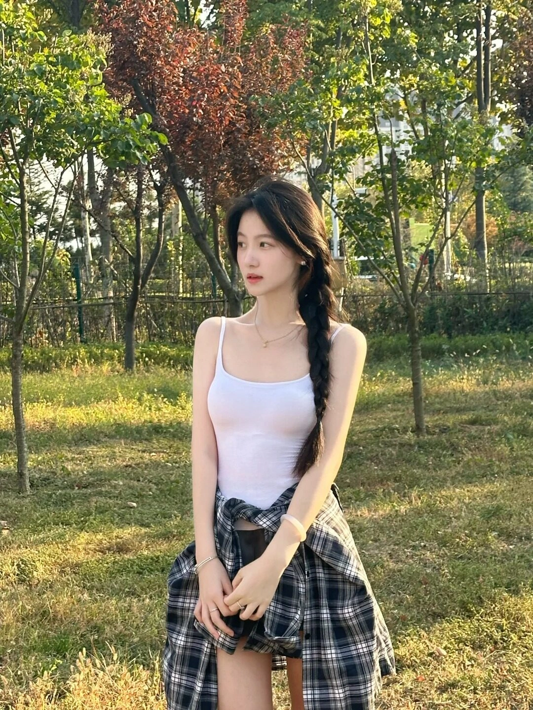 Tóc tết lệch duyên dáng, áo hai dây trắng tinh khôi giữa không gian thiên nhiên xanh mát.