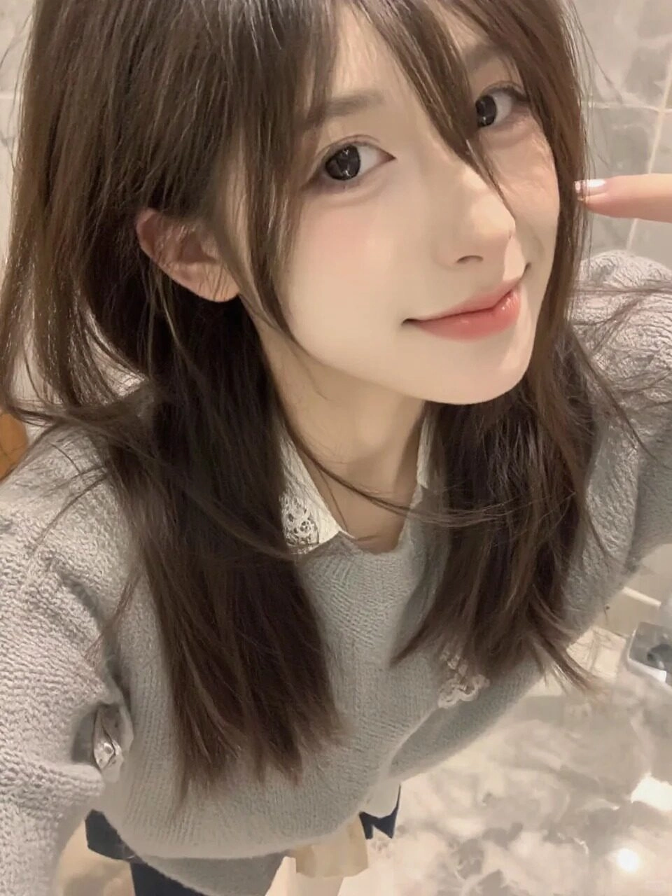 Tóc dài suôn mượt, áo len xám kết hợp sơ mi trắng tạo vẻ ngoài thanh lịch.