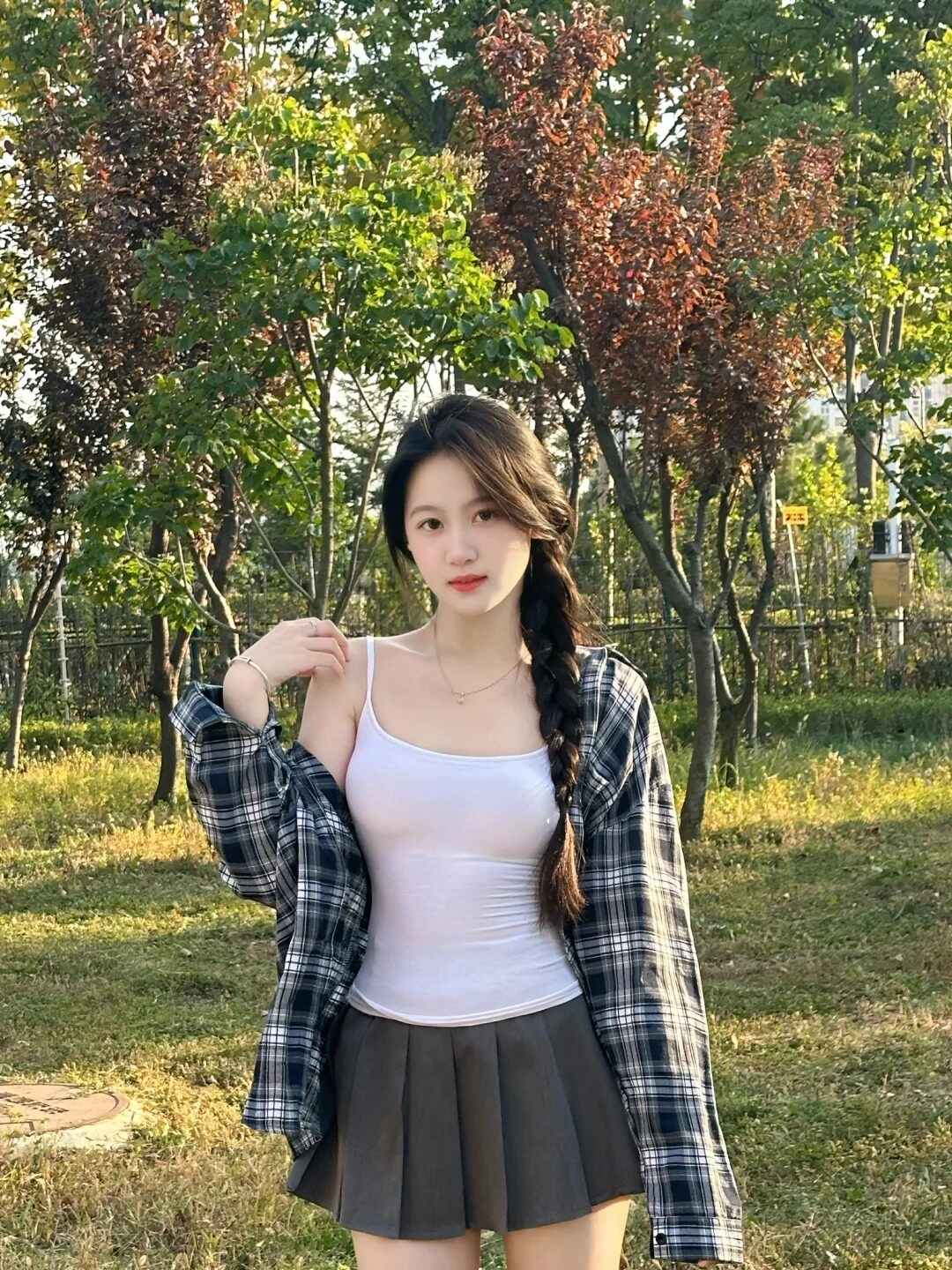 Tóc tết lệch một bên, váy ngắn và áo hai dây trắng giữa không gian xanh mát.