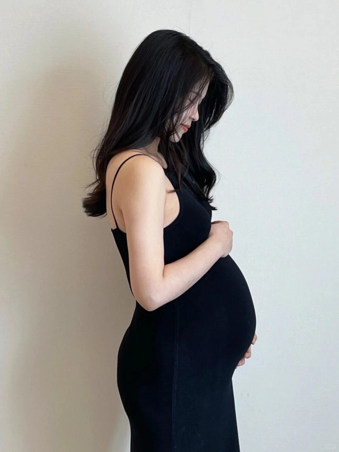 Váy đen ôm sát, tay nhẹ nhàng đặt lên bụng, mẹ bầu đầy dịu dàng và yêu thương.