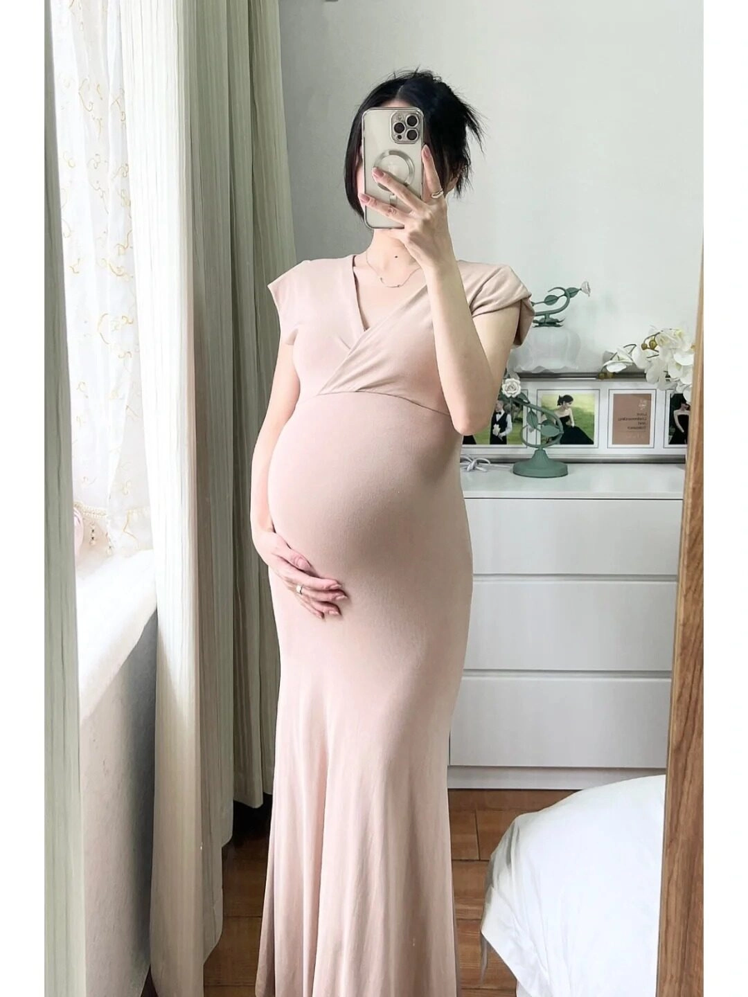 Váy dài nude ôm sát cơ thể, mẹ bầu nhẹ nhàng đặt tay lên bụng, tràn đầy yêu thương.