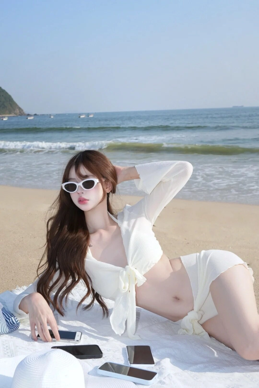 Cô gái đeo kính râm, mang bộ đồ màu trắng khoe body nóng bỏng trên bờ biển.