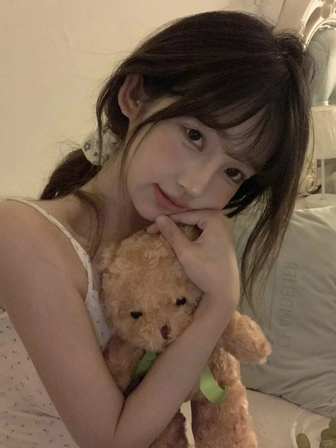 Ôm gấu bông trong lòng, ánh mắt nhẹ nhàng đầy cảm xúc giữa không gian ấm áp.