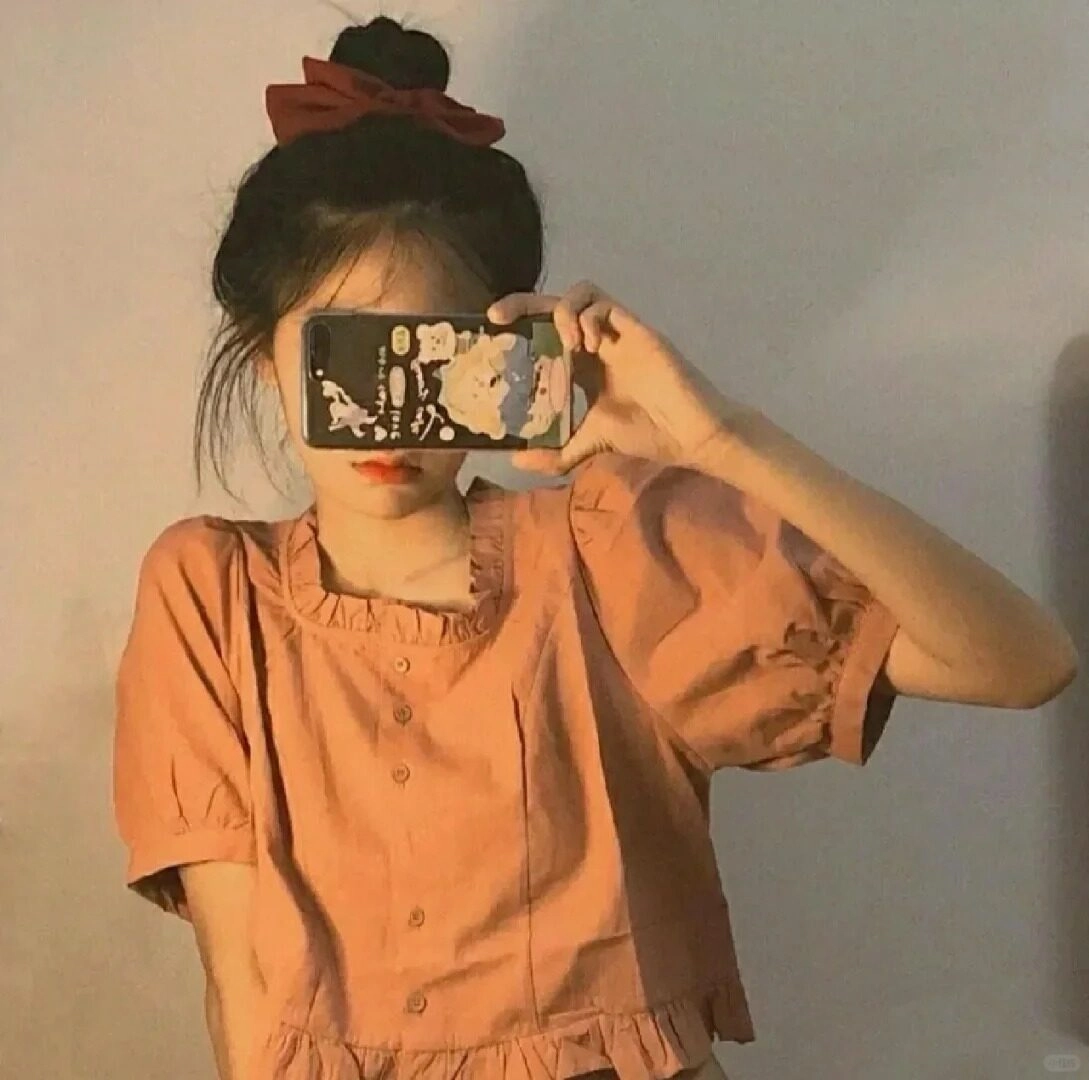 Tóc búi cao, áo cam nhẹ nhàng, tay che mặt đầy dễ thương