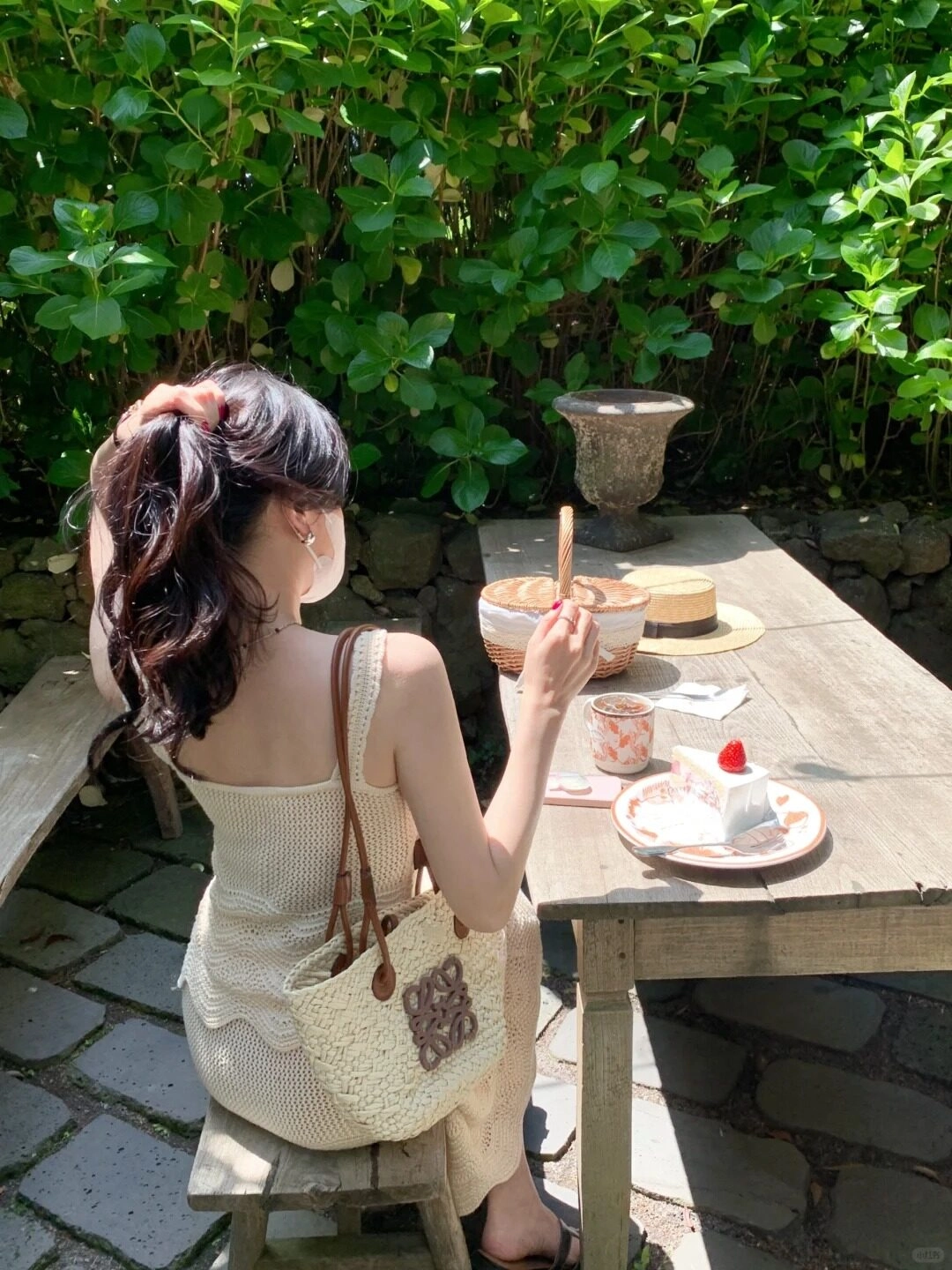 Ngồi ngoài trời, buộc tóc hờ hững, diện váy len trắng cùng túi đan thủ công.