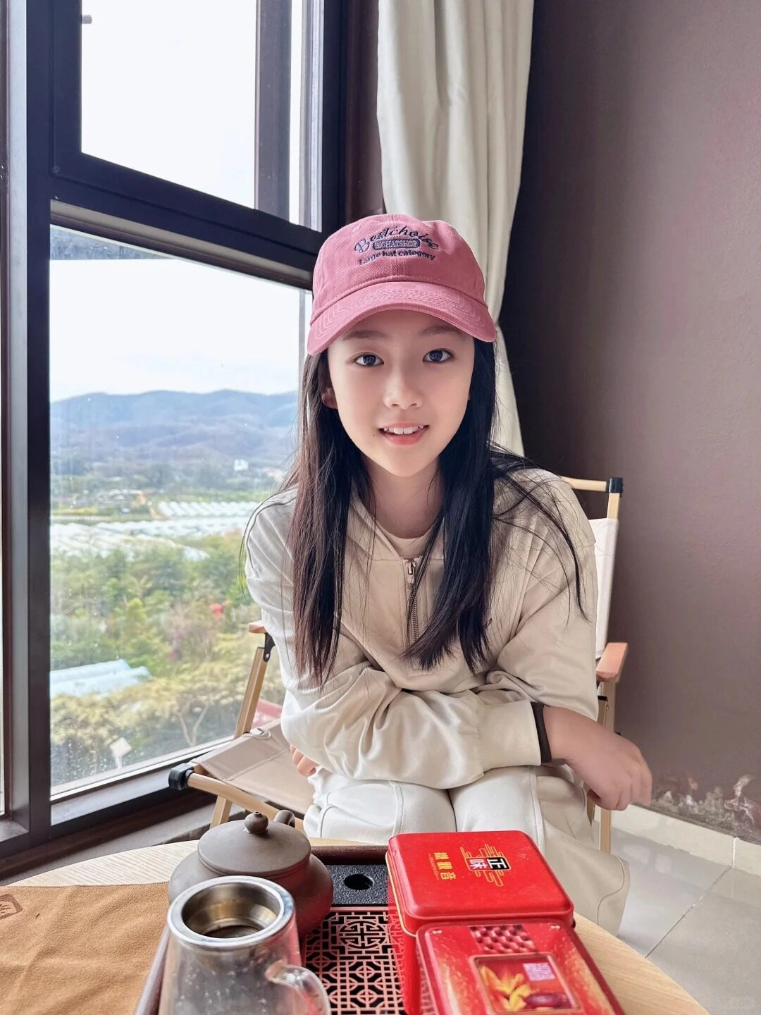 Cô gái nhỏ lớp 5 đáng yêu đội mũ hồng ngồi thưởng trà bên cửa sổ.