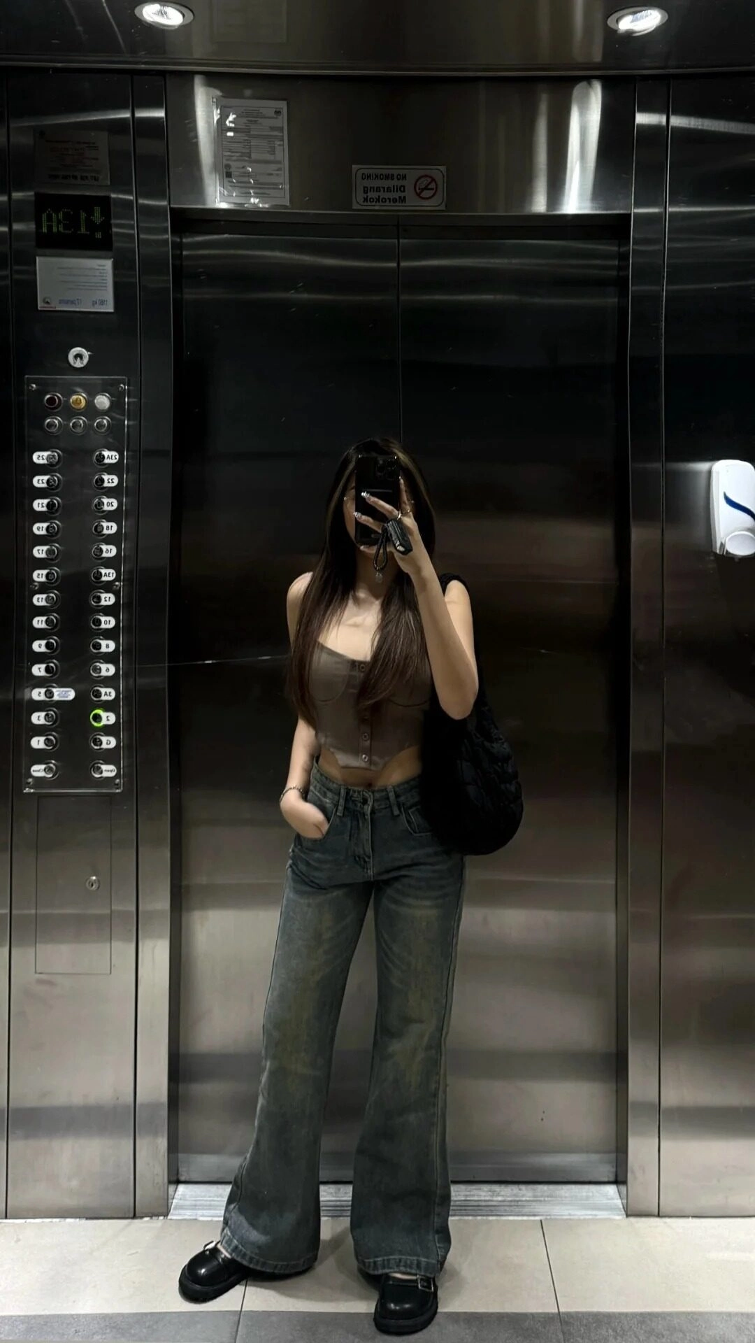 Áo croptop, quần jean ống rộng, tay trái bỏ túi, chụp ảnh trong thang máy.