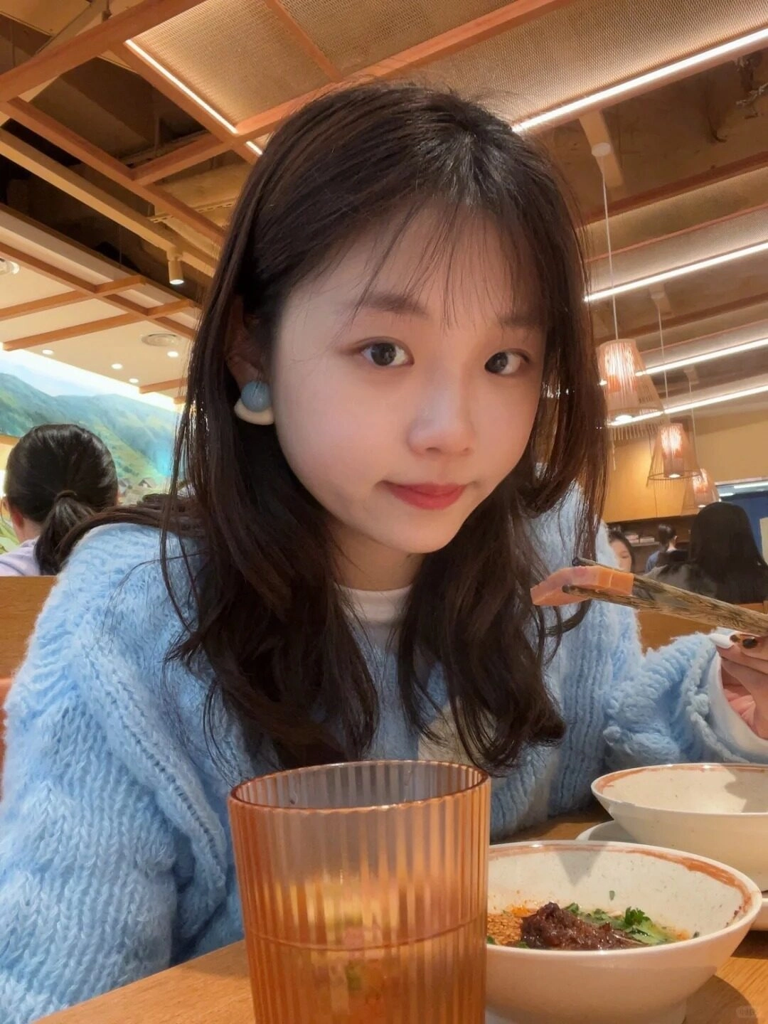 Cô gái đáng yêu mang áo len xanh, thưởng thức bữa ăn vui vẻ tại quán ăn.