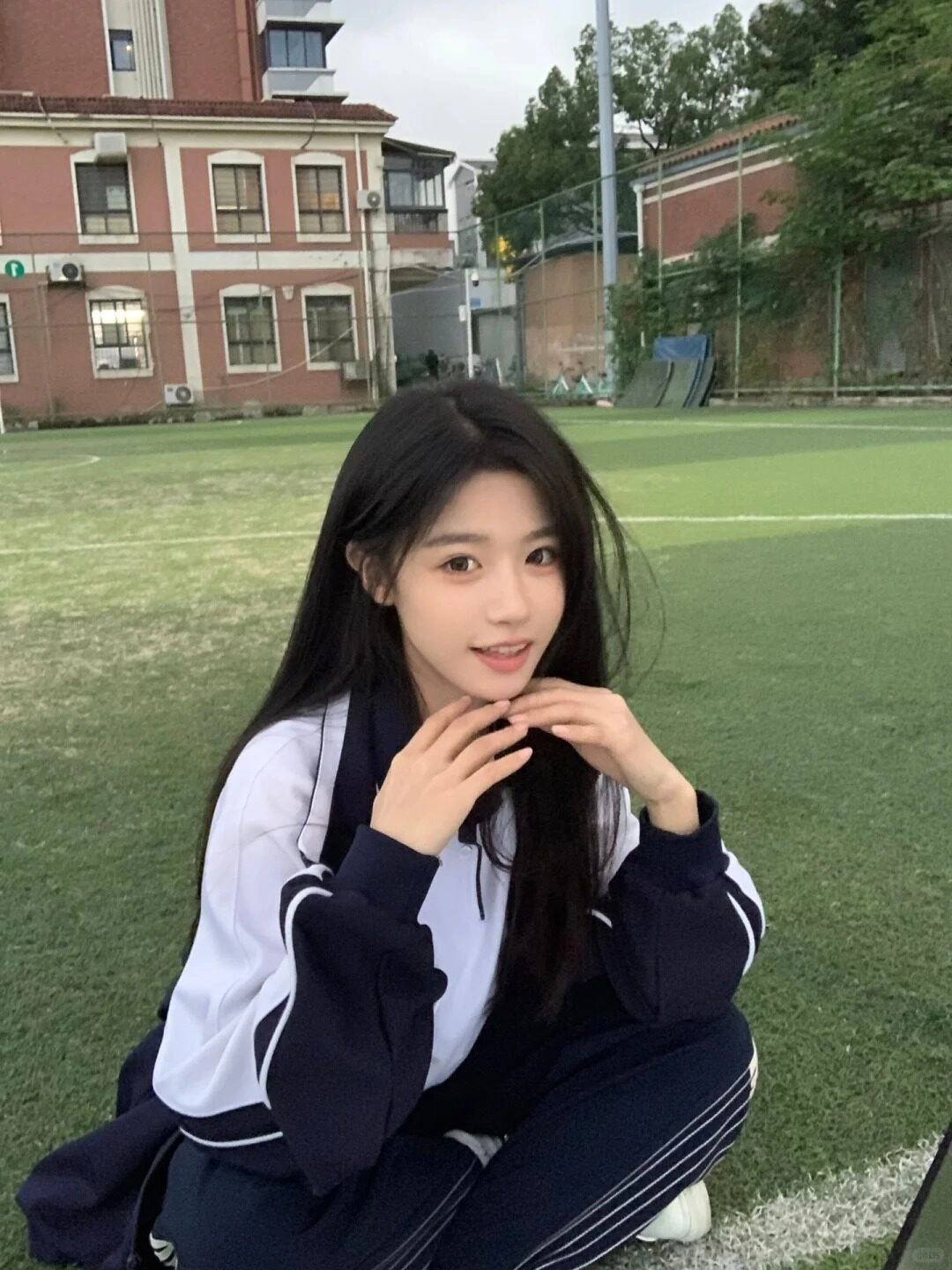 Em học sinh xinh xắn mang đồng phục tạo dáng ngoài sân bóng