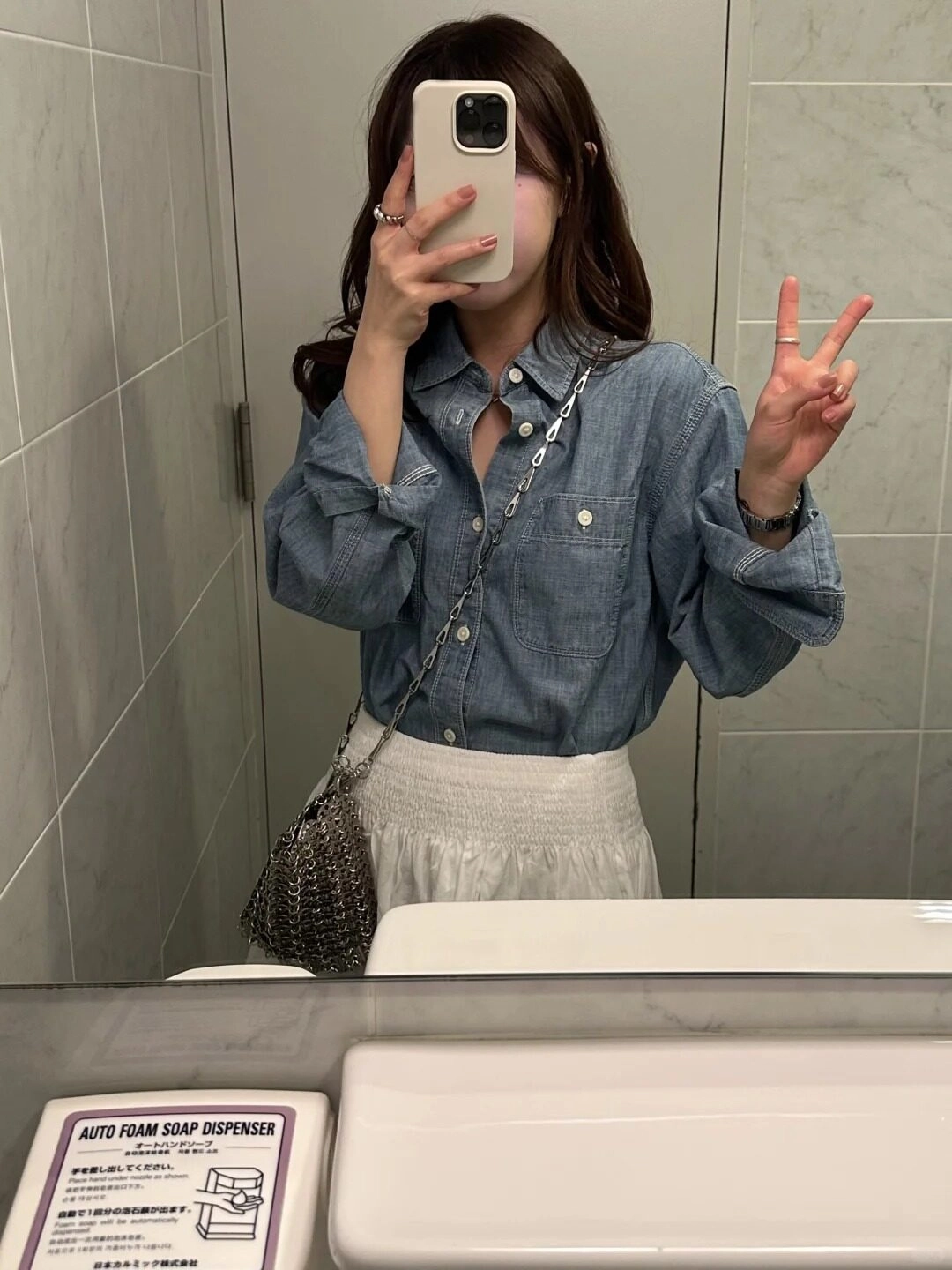 Áo sơ mi denim, váy chân trắng, tạo kiểu dáng chữ V tinh nghịch, tóc xoăn nhẹ.