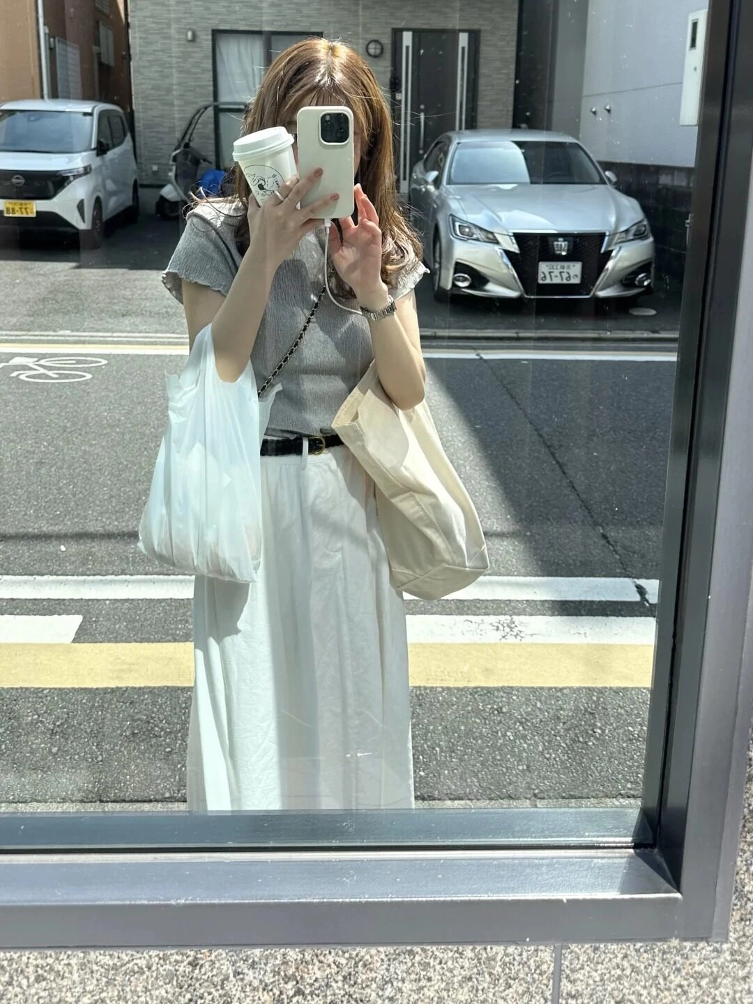 Chụp kính ngoài trời, tóc xoăn nhẹ, áo xám phối chân váy trắng nữ tính.