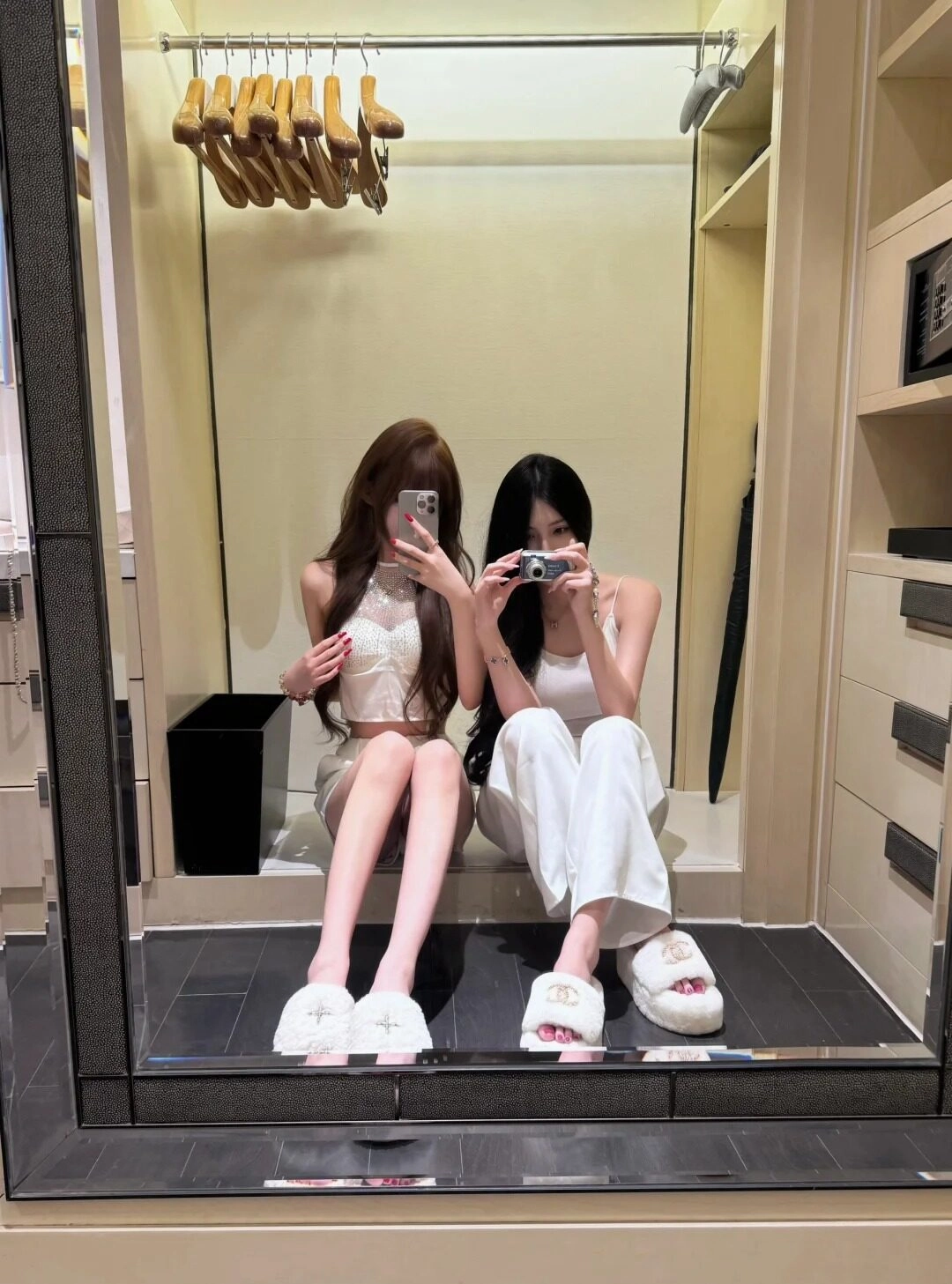 Hai cô gái ngồi trên sàn, đồ trắng, tạo kiểu dáng selfie vui vẻ trước ống kính.