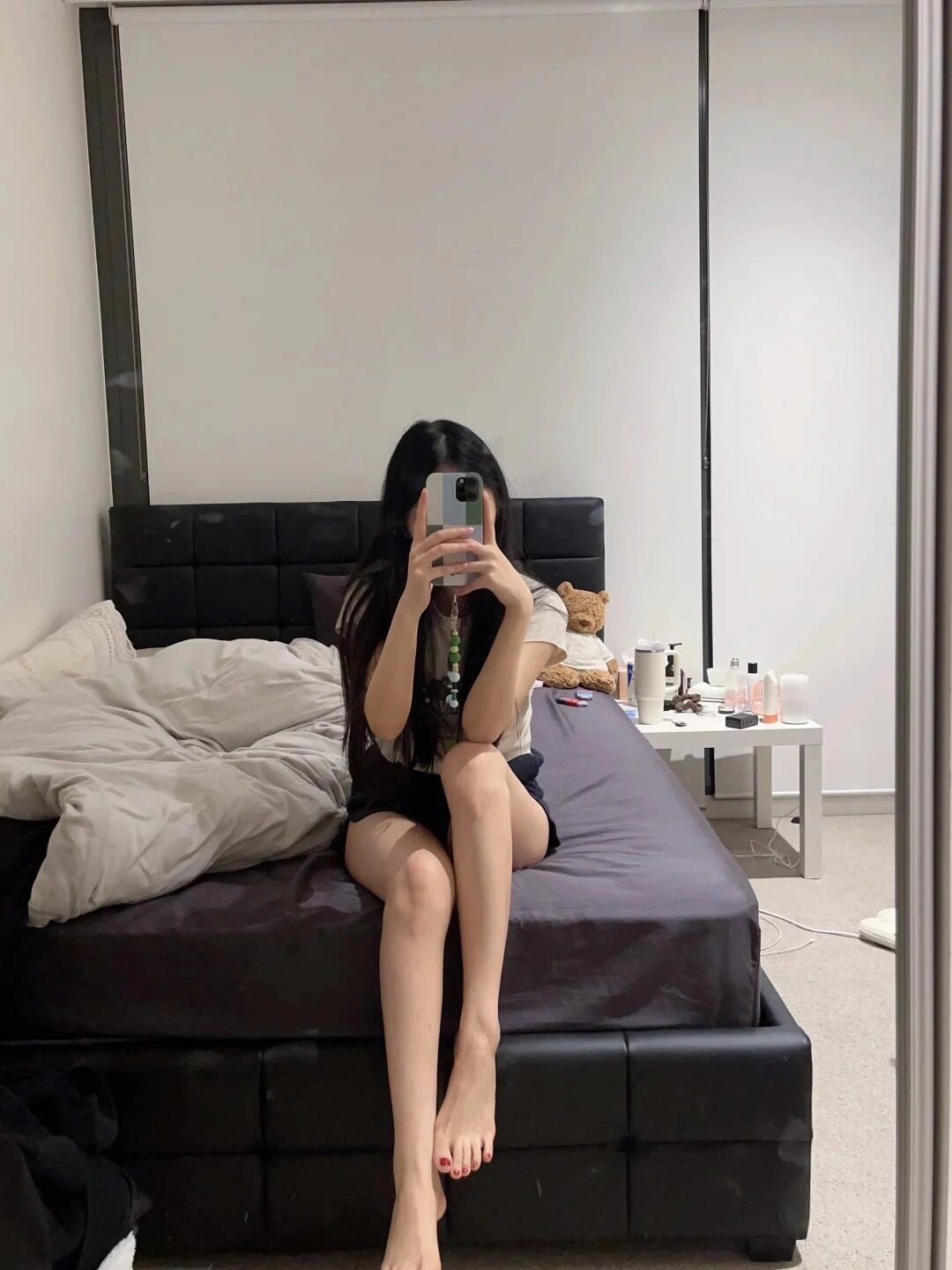 Ngồi trên giường, che mặt bằng điện thoại, chân thon dài trong phòng ngủ.