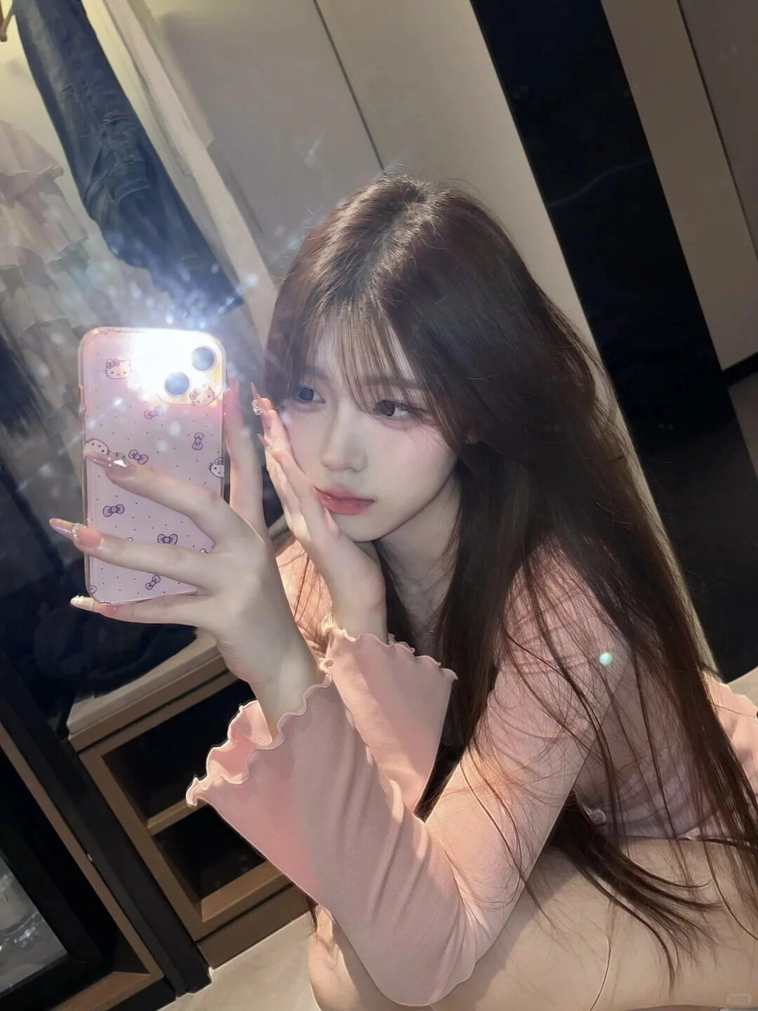 Cô gái áo hồng tay dài selfie trước ống kính, tóc dài xõa mềm nữ tính.