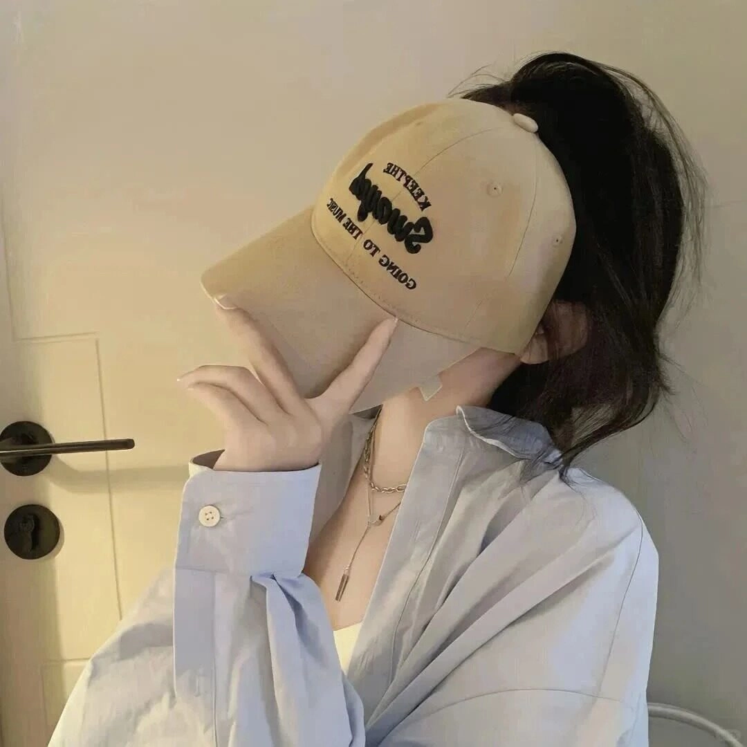  Đội mũ lưỡi trai be, che mặt bằng tay, diện sơ mi xanh nhẹ nhàng.