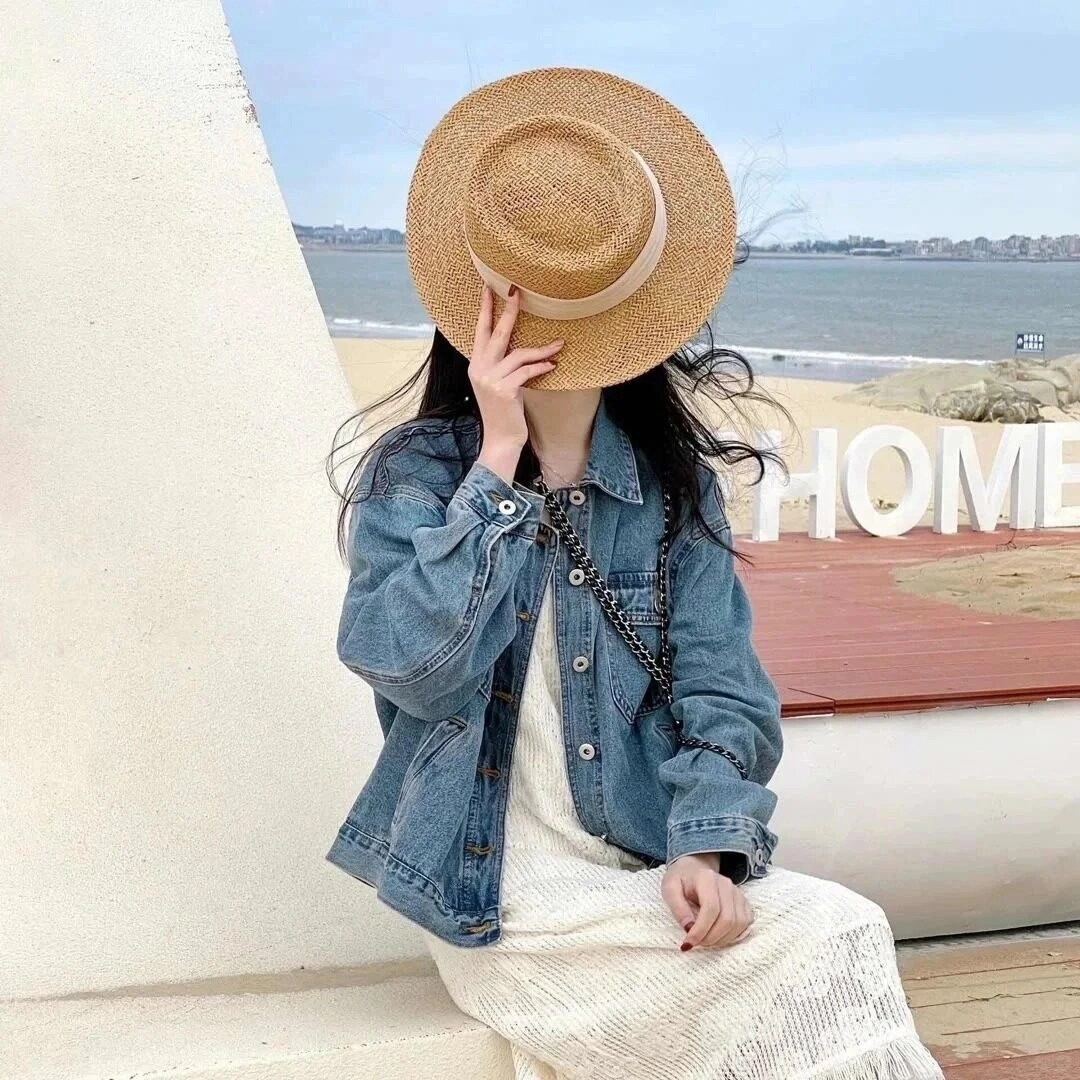 Giấu mặt sau mũ cói, diện váy trắng và áo khoác denim bên bờ biển.