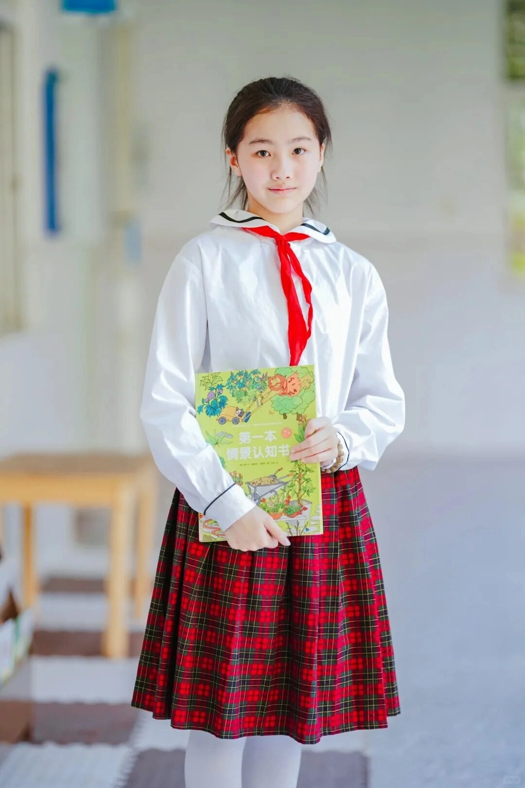 Nữ sinh thanh lịch cầm sách trên tay, tự tin đứng giữa sân trường.