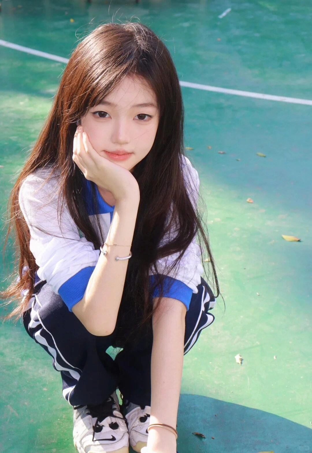 Nữ sinh chống suy tư, tóc xõa dài dịu dàng, ngồi sân trường xanh mát.