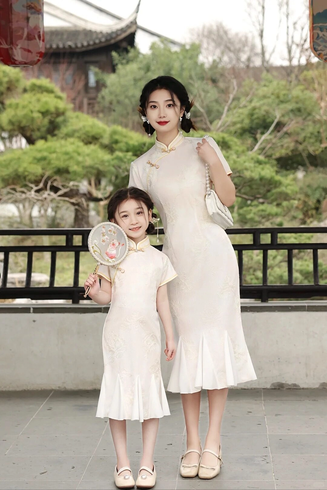 Mẹ và con trong sườn xám đôi, bé cầm quạt thêu xinh xắn, toát lên vẻ truyền thống.