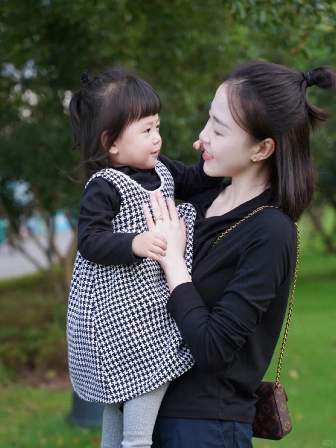 Mẹ diện áo đen, con mặc váy kẻ caro đen trắng, ánh mắt đầy yêu thương.