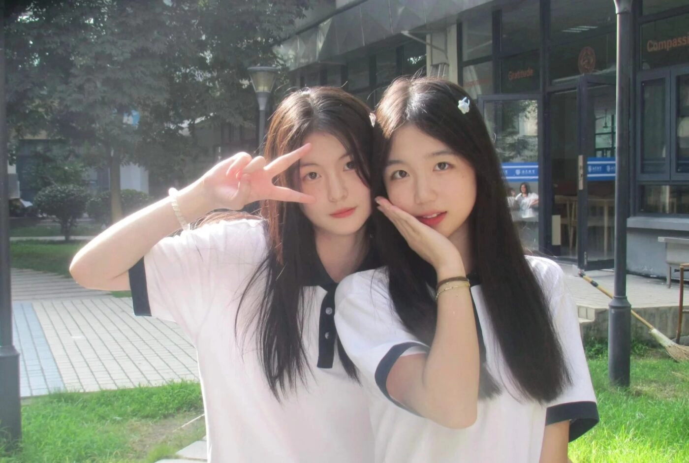 Hai bạn gái mặc áo đồng phục dễ thương, tóc buông dài, tạo kiểu dáng vui vẻ.