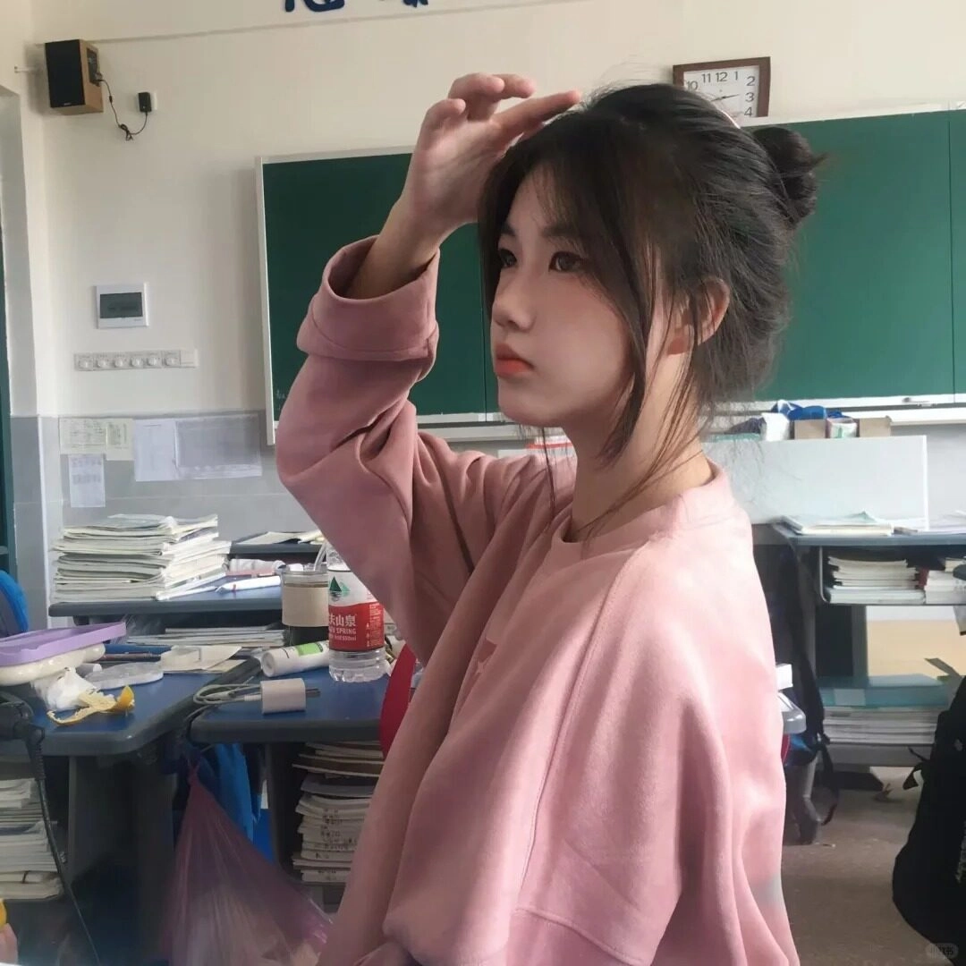 Cô gái 2k10 áo hồng, búi tóc gọn gàng, chỉnh tóc trong lớp học.