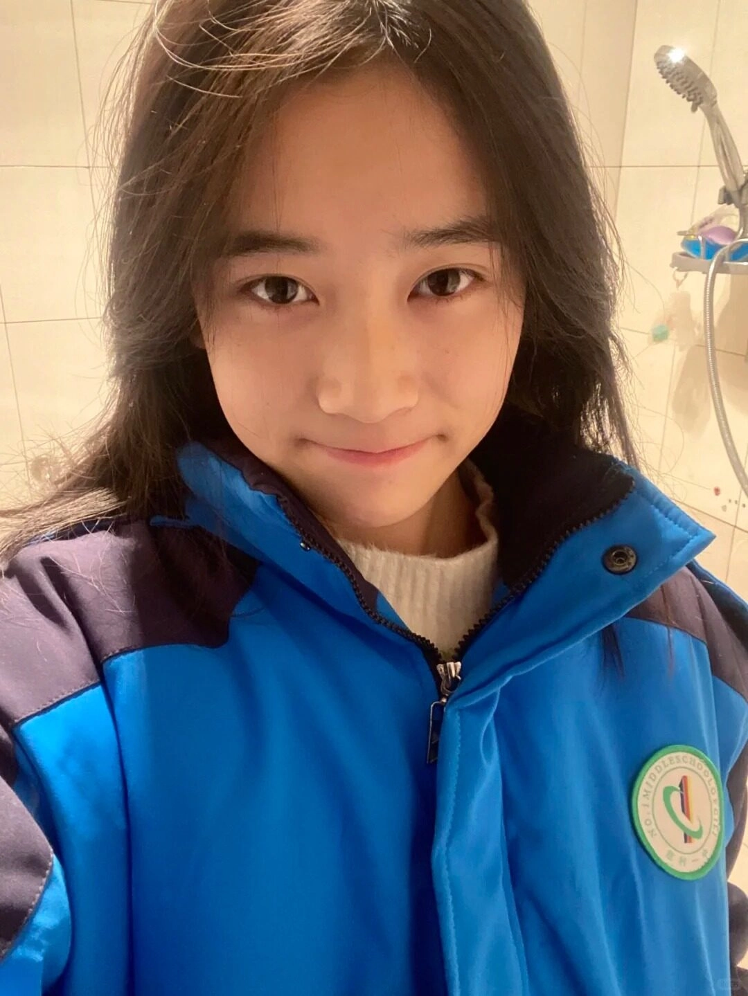 Nữ sinh mặc áo khoác đồng phục xanh dương, tóc tự nhiên, biểu cảm thân thiện.