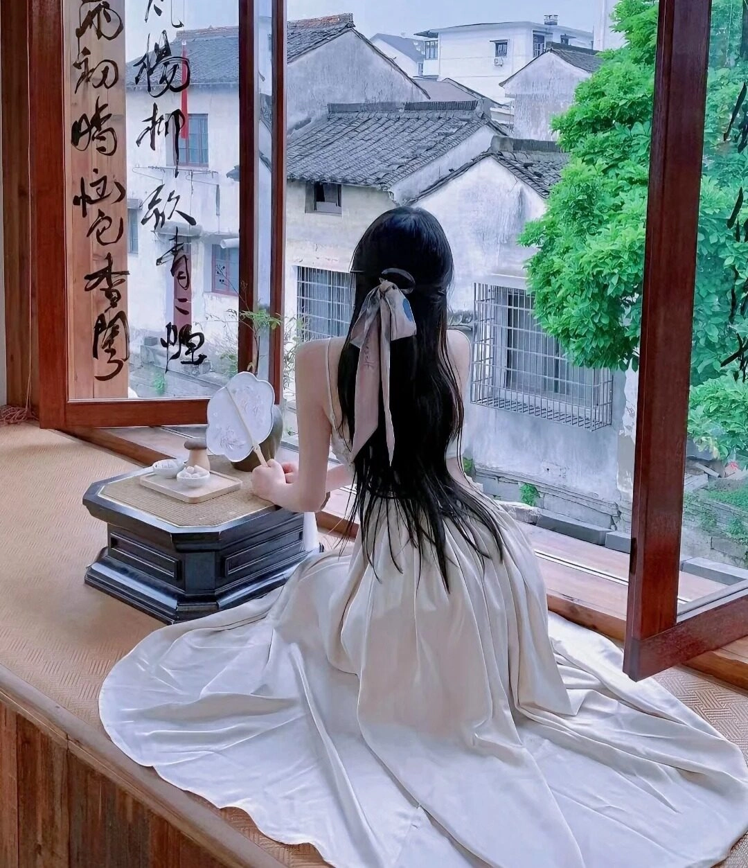 Thiếu nữ váy dài màu kem ngồi bên cửa sổ ngắm phố cổ.