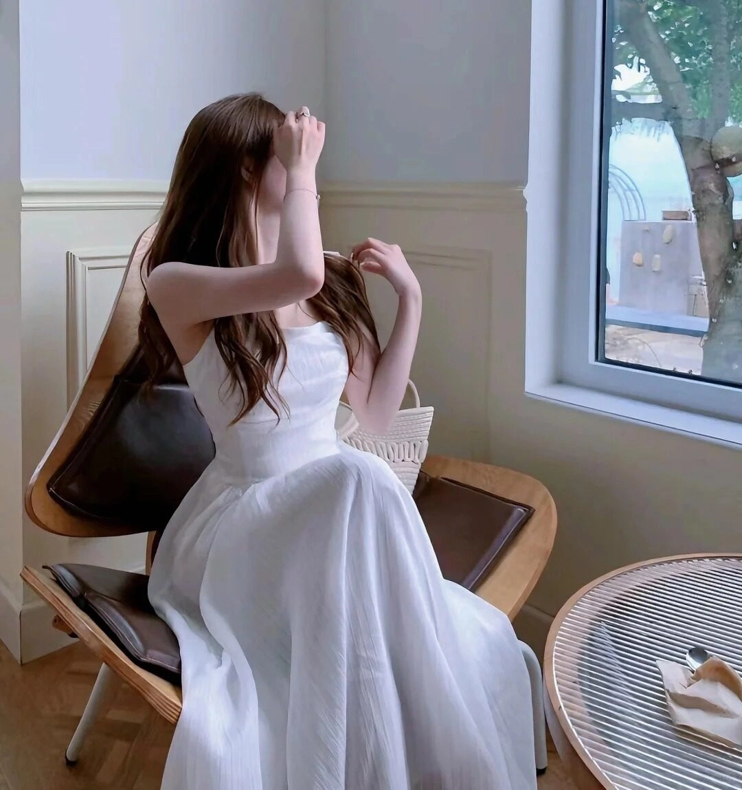 Cô gái duyên dáng trong váy trắng, ngồi ghế gỗ, che mặt e thẹn.