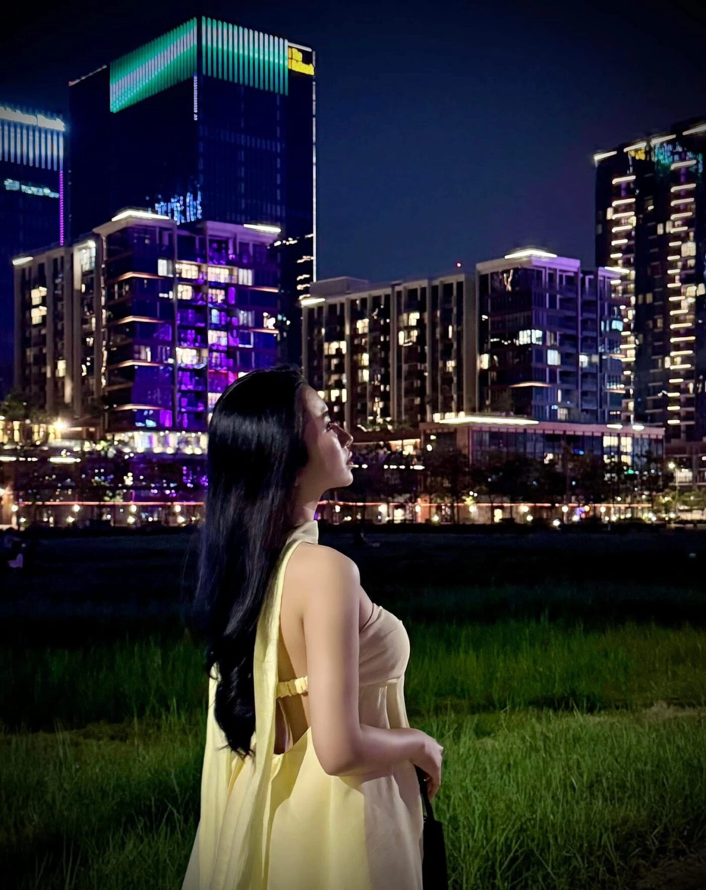 Cô nàng với mái tóc đen dài đứng nhìn thành phố về đêm, Váy vàng bồng bềnh nổi bật."