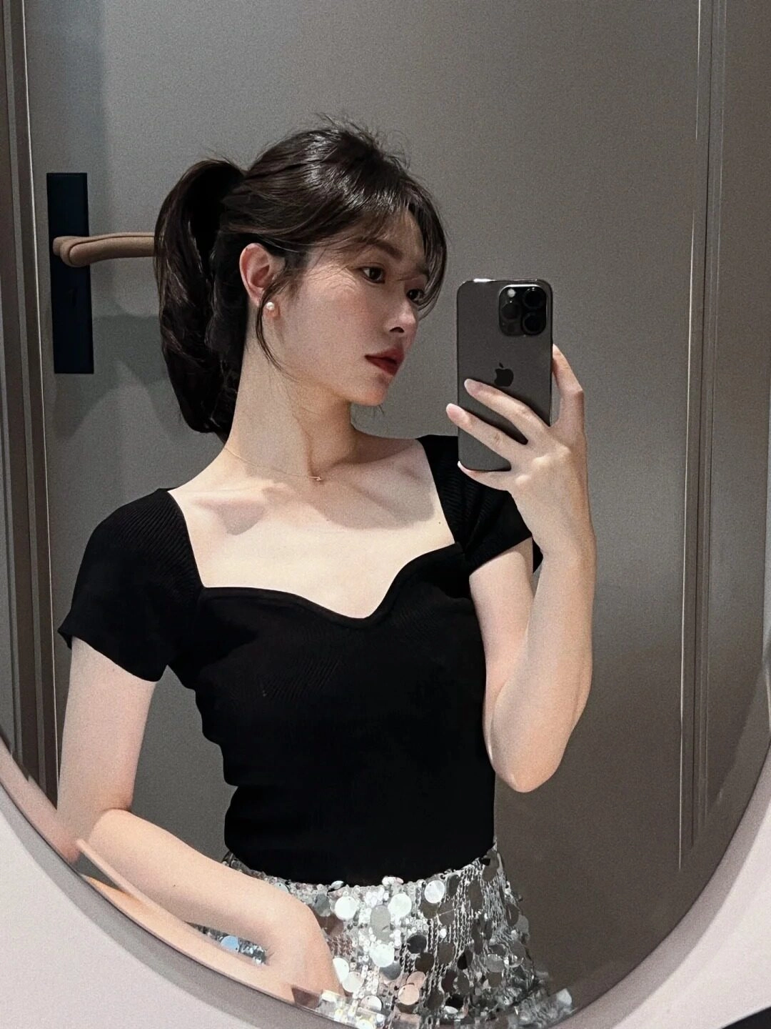 Tóc cột cao thanh lịch, áo đen đơn giản chân váy ánh bạc nổi bật.