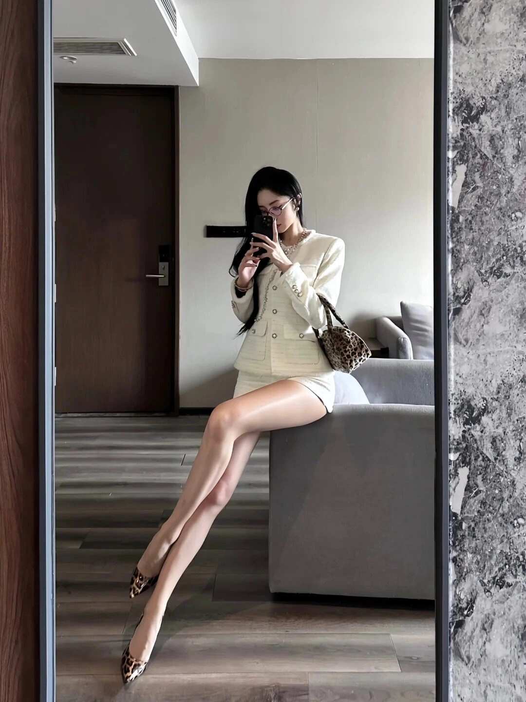 Tóc dài duỗi thẳng, áo vest trắng thanh lịch, chân dài nổi bật trước gương.