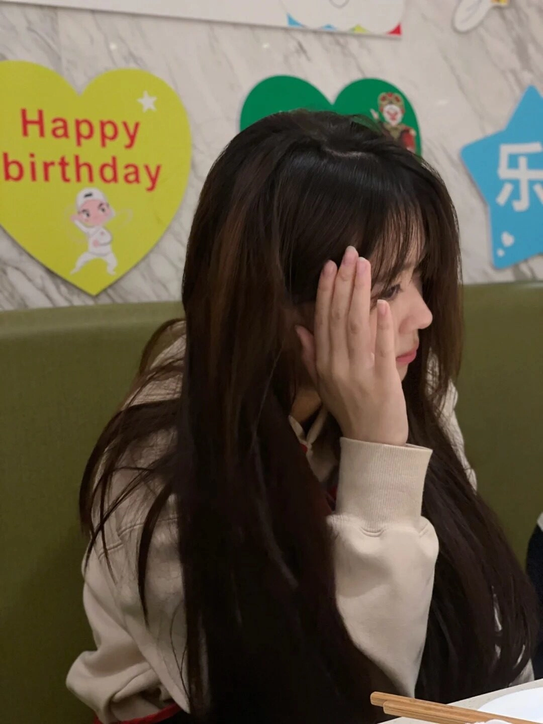 Thiếu nữ tóc dài buông xõa, chống tay suy tư cạnh bảng "Happy Birthday".