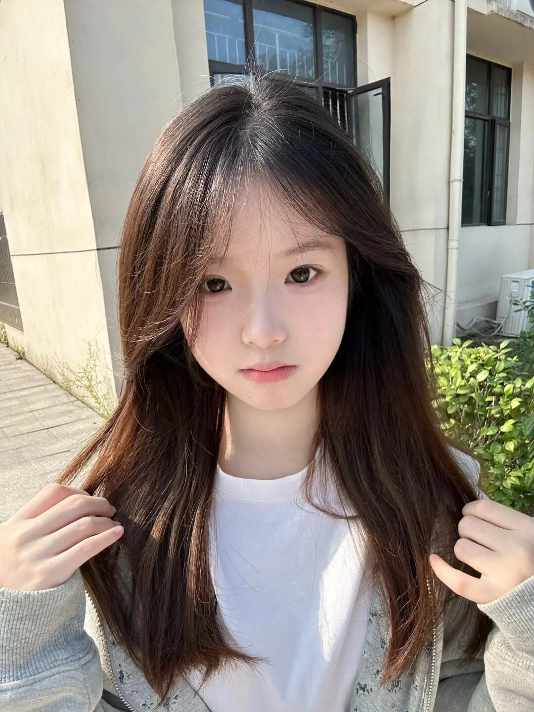 Cô gái tóc dài tự nhiên, trang phục đơn giản, tay vuốt tóc nhẹ nhàng.