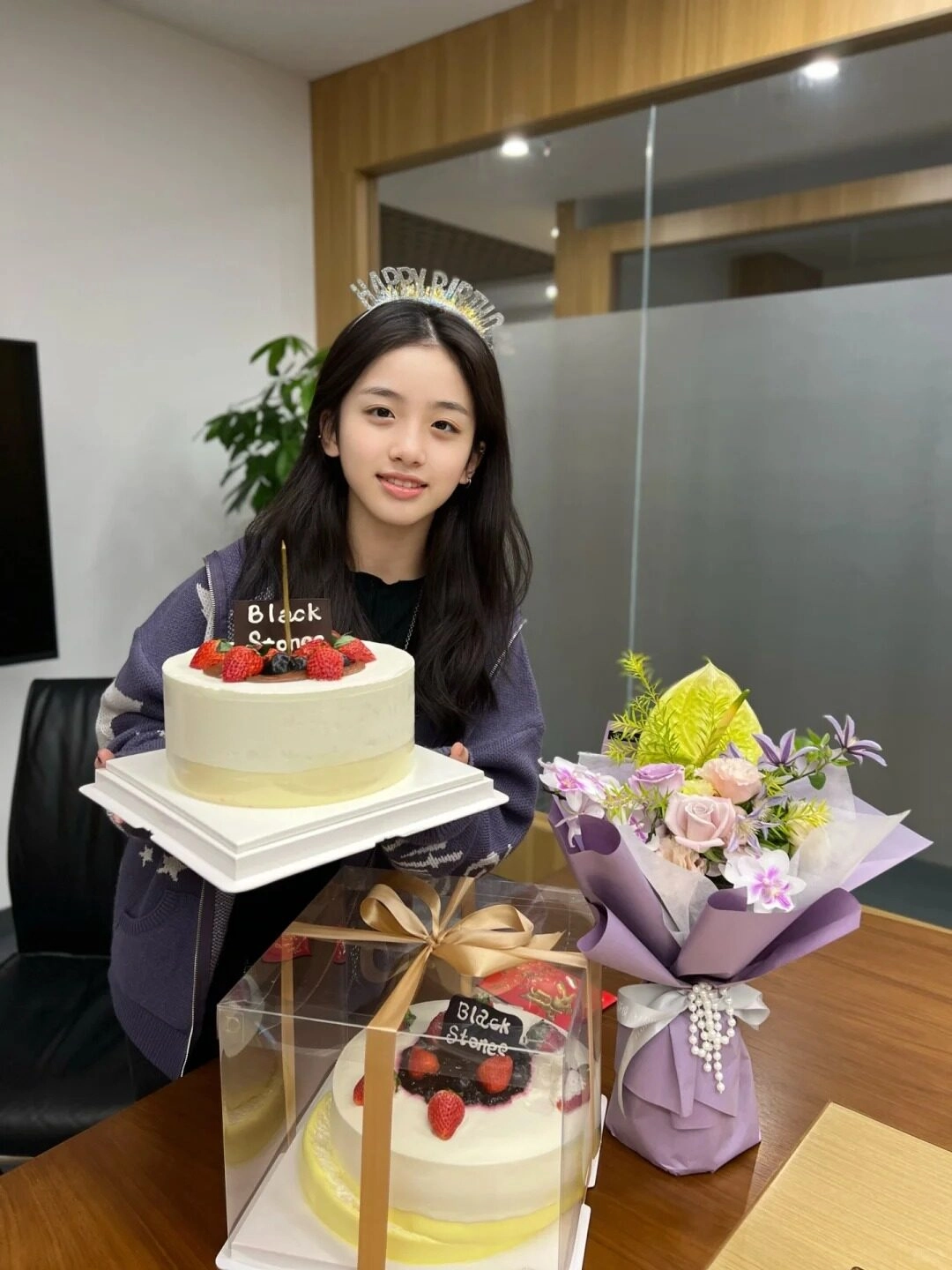 Cô gái mặc áo khoác xám xanh, vui vẻ ôm bánh sinh nhật tuổi 15