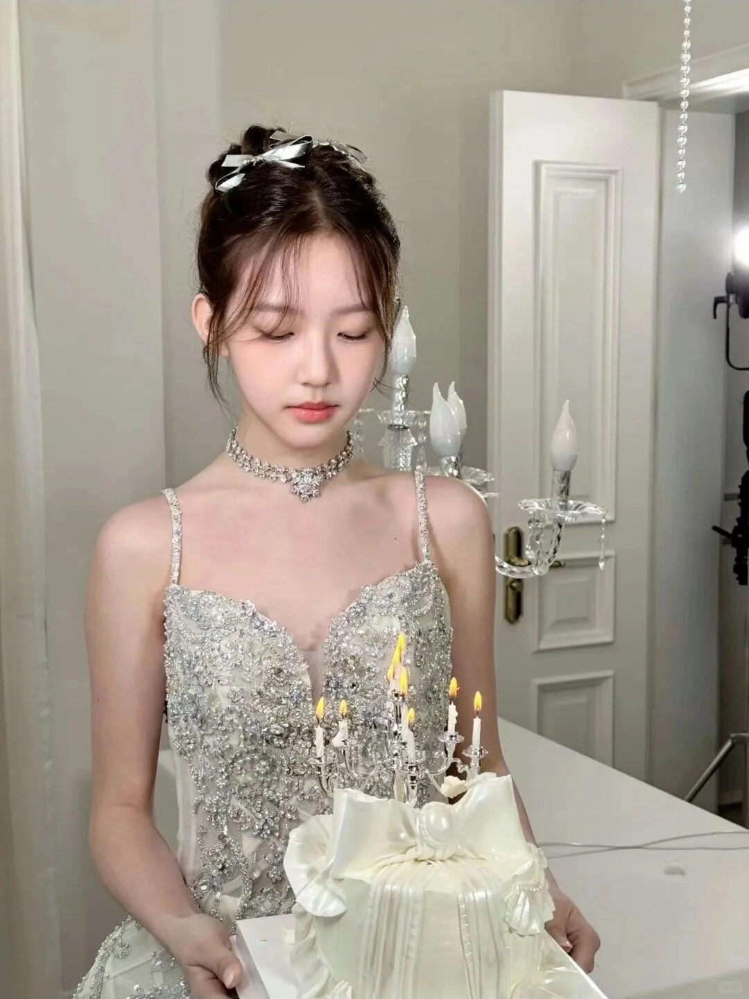 Cô gái mặc váy dạ hội đính đá sang trọng, tóc búi cài nơ, cầm bánh sinh nhật.