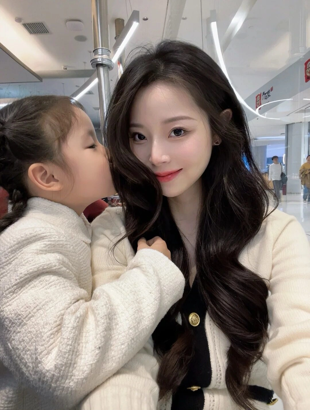Con gái hôn lên tóc mẹ, áo len trắng tạo nên khoảnh khắc đầy yêu thương.