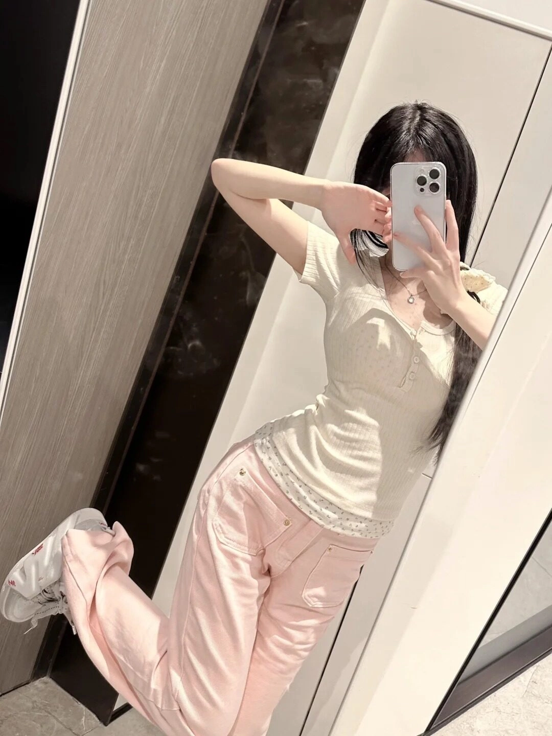 Che mặt bằng điện thoại, diện áo trắng ôm sát và quần hồng pastel nhẹ nhàng.
