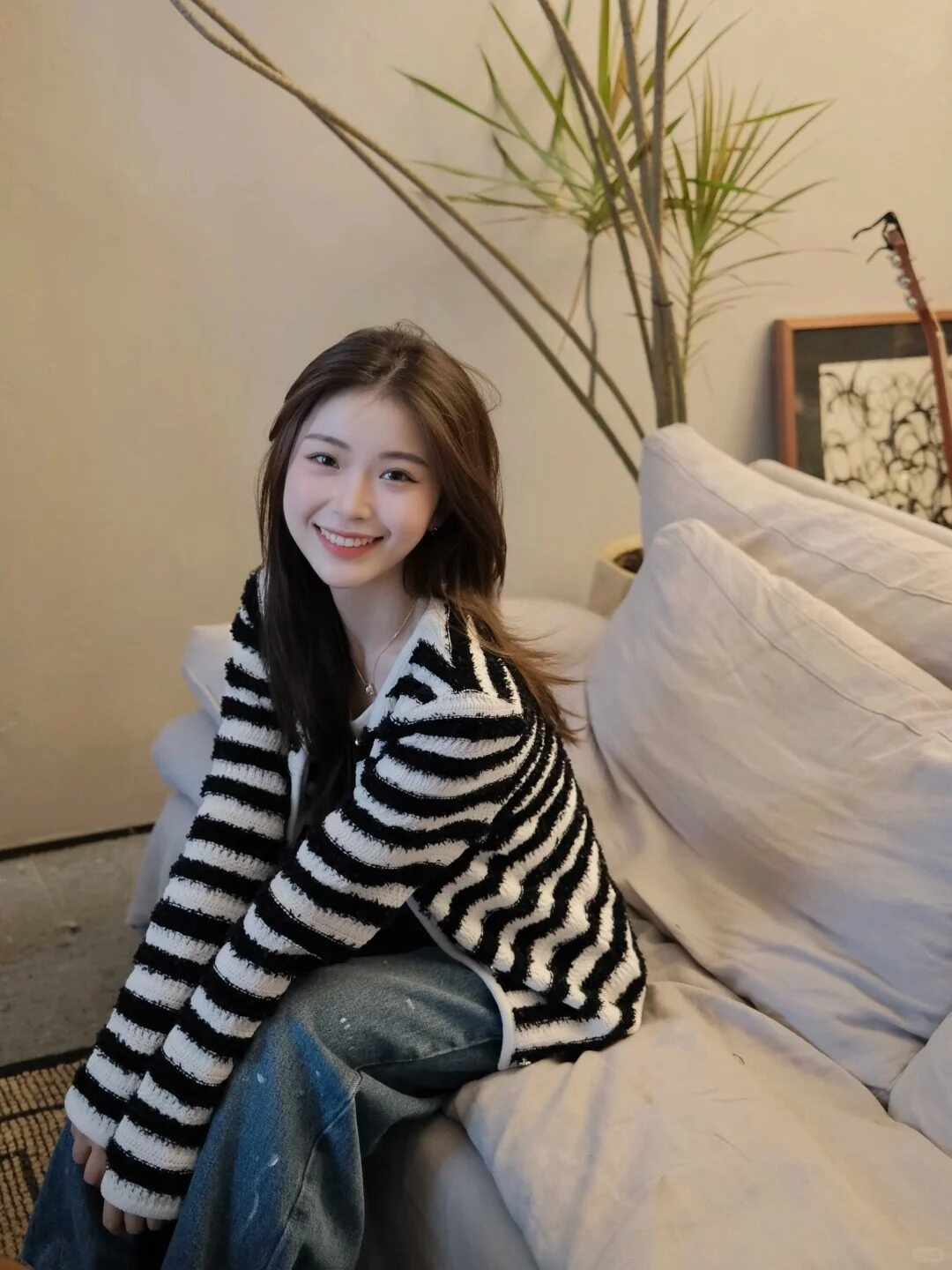 Cô gái nự cười tươi sáng với mái tóc dài nâu tạo dáng trên sofa.