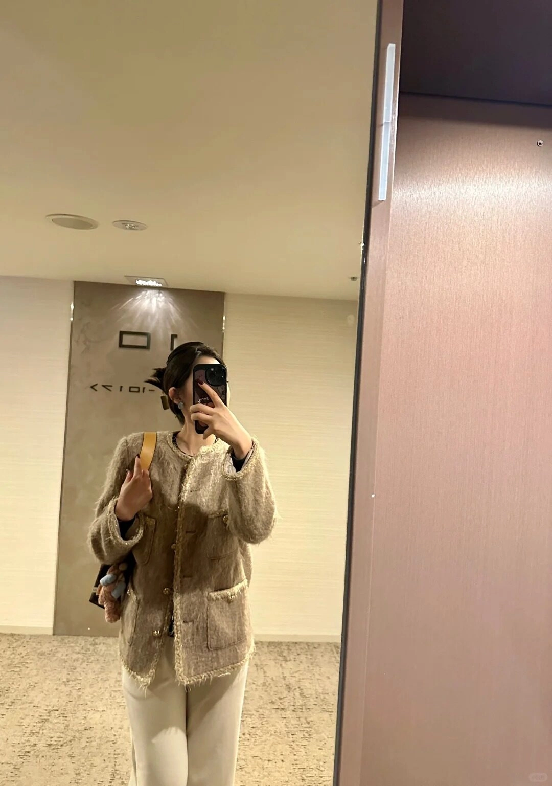 Kiểu tóc búi thấp, mặc áo khoác ngoài rộng rãi tạo hình trước gương.